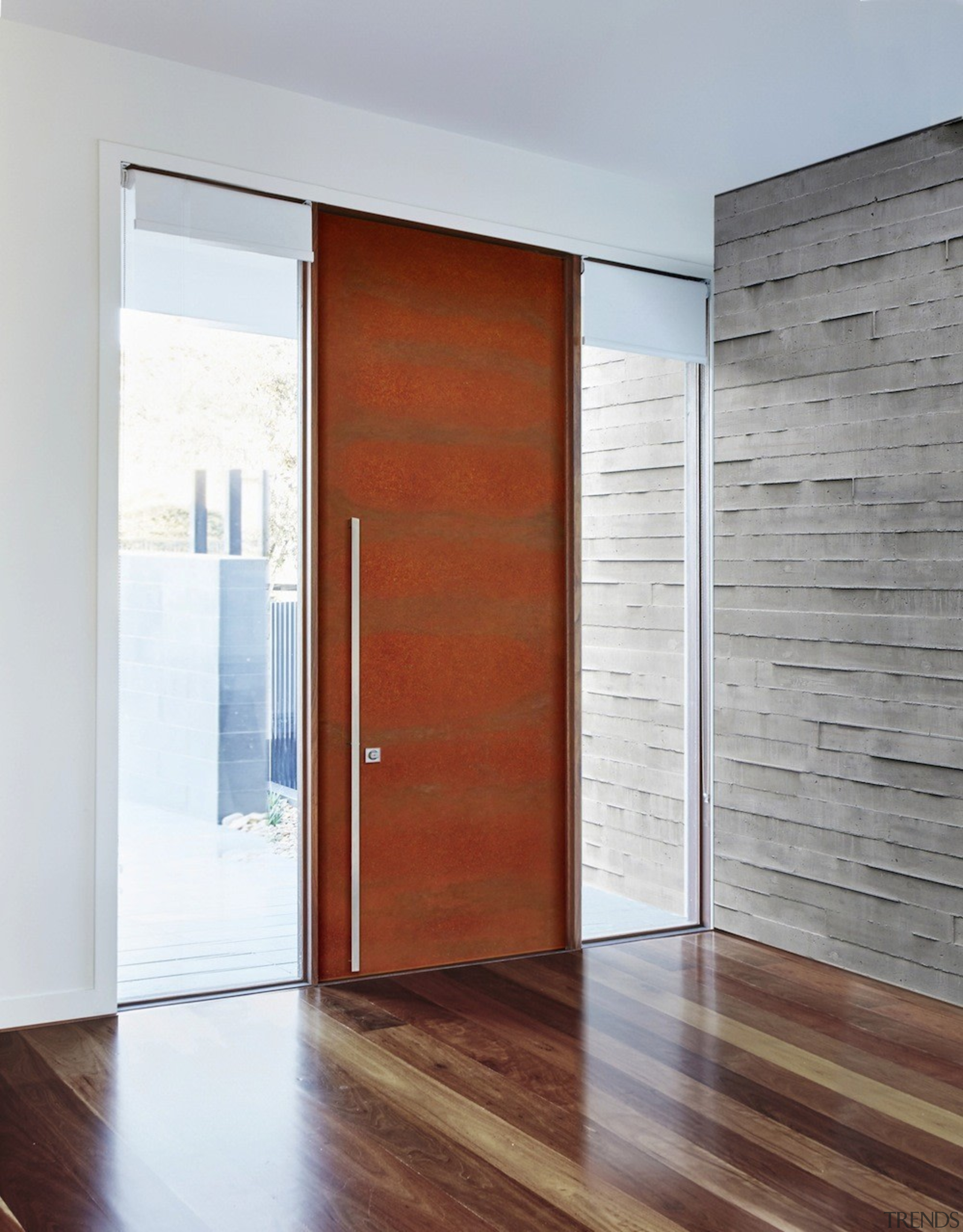 A weathering steel door contrasts with the concrete door, floor, interior design, wood, wood stain, gray, white