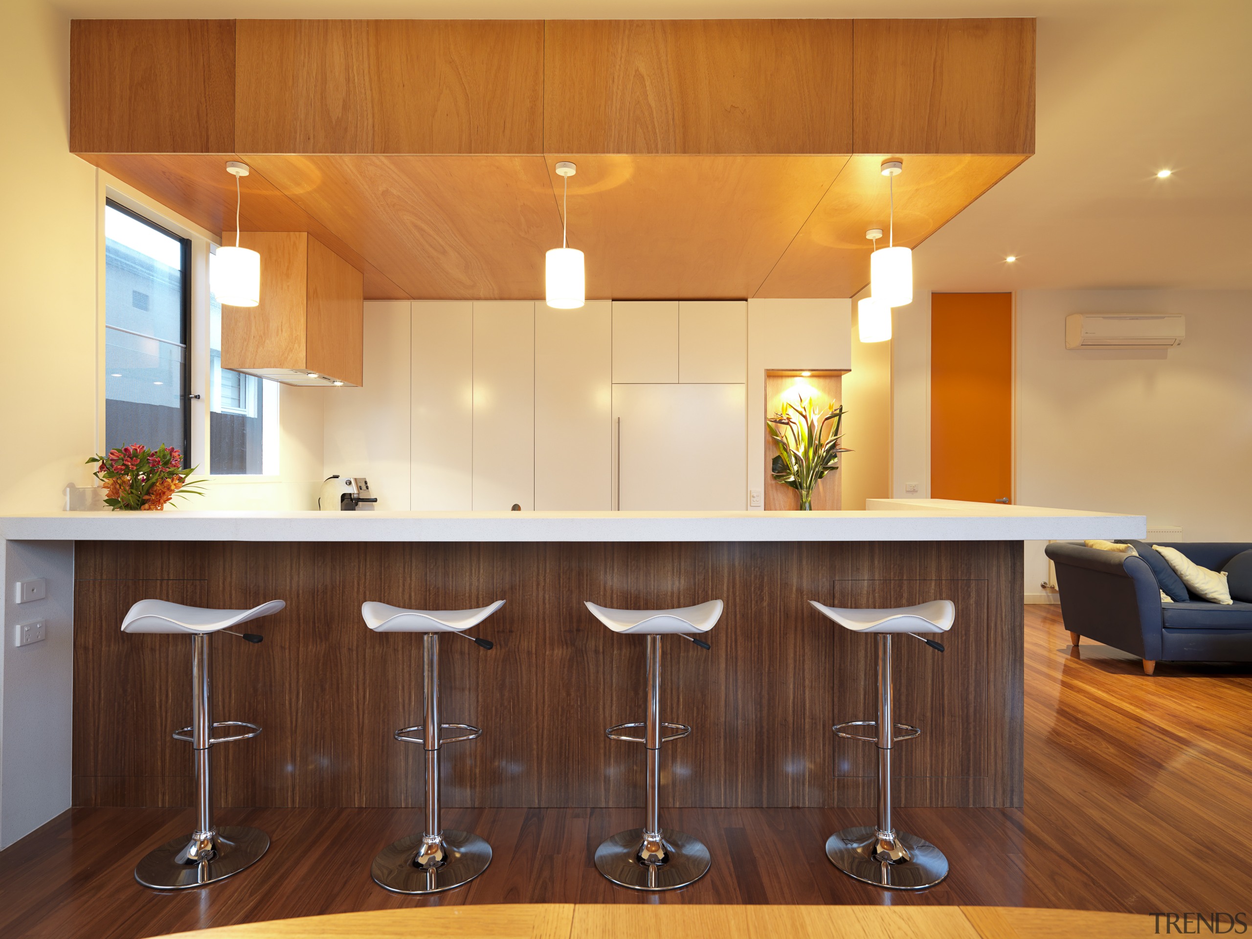 View of kitchen area featuring an island with cabinetry, ceiling, countertop, flooring, hardwood, home, interior design, kitchen, lighting, real estate, room, under cabinet lighting, wood, brown, orange