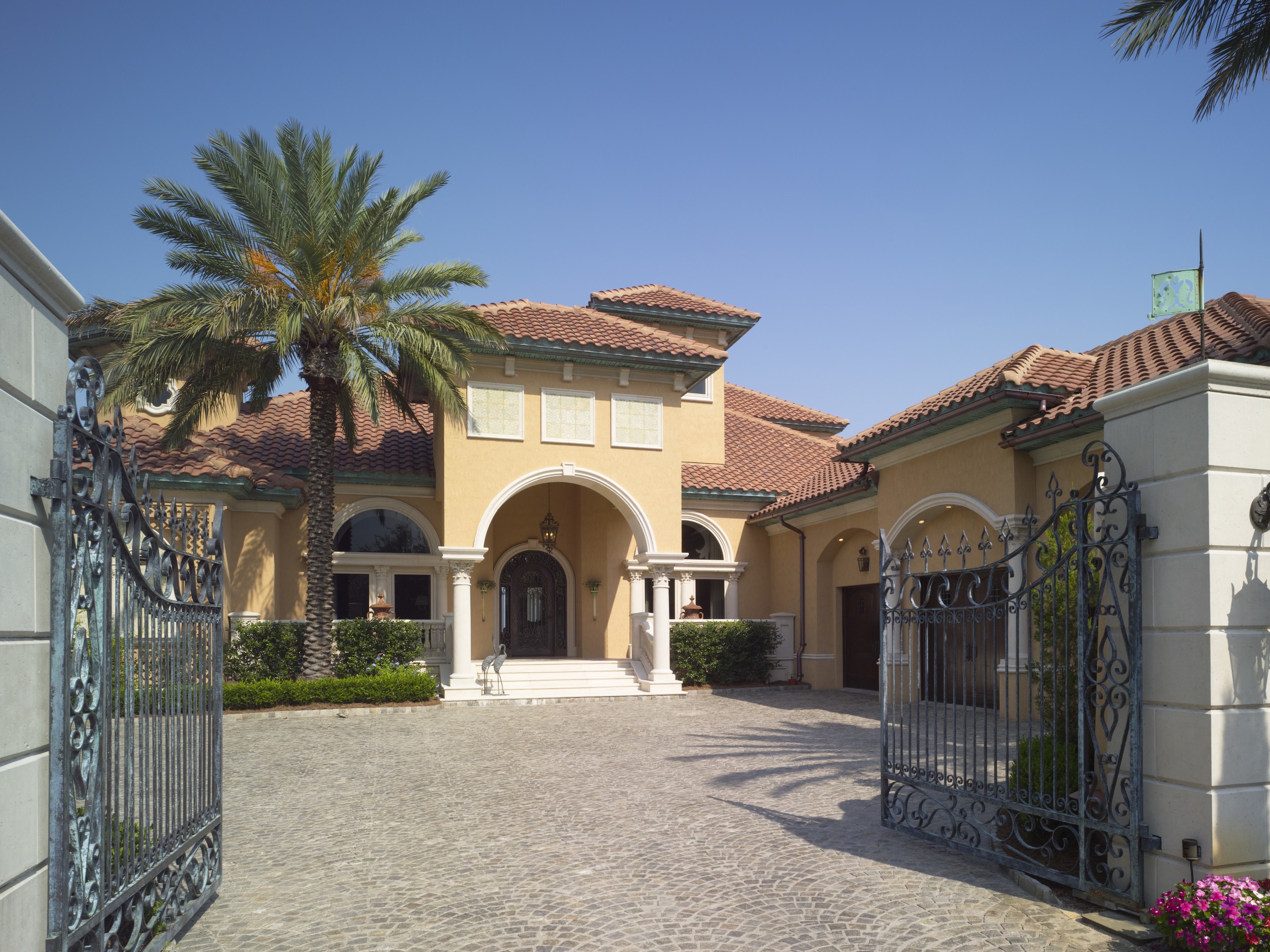 Exterior view of an Italian villa-styled waterfront home. arecales, building, estate, facade, hacienda, home, house, mansion, palm tree, property, real estate, residential area, villa, gray, teal