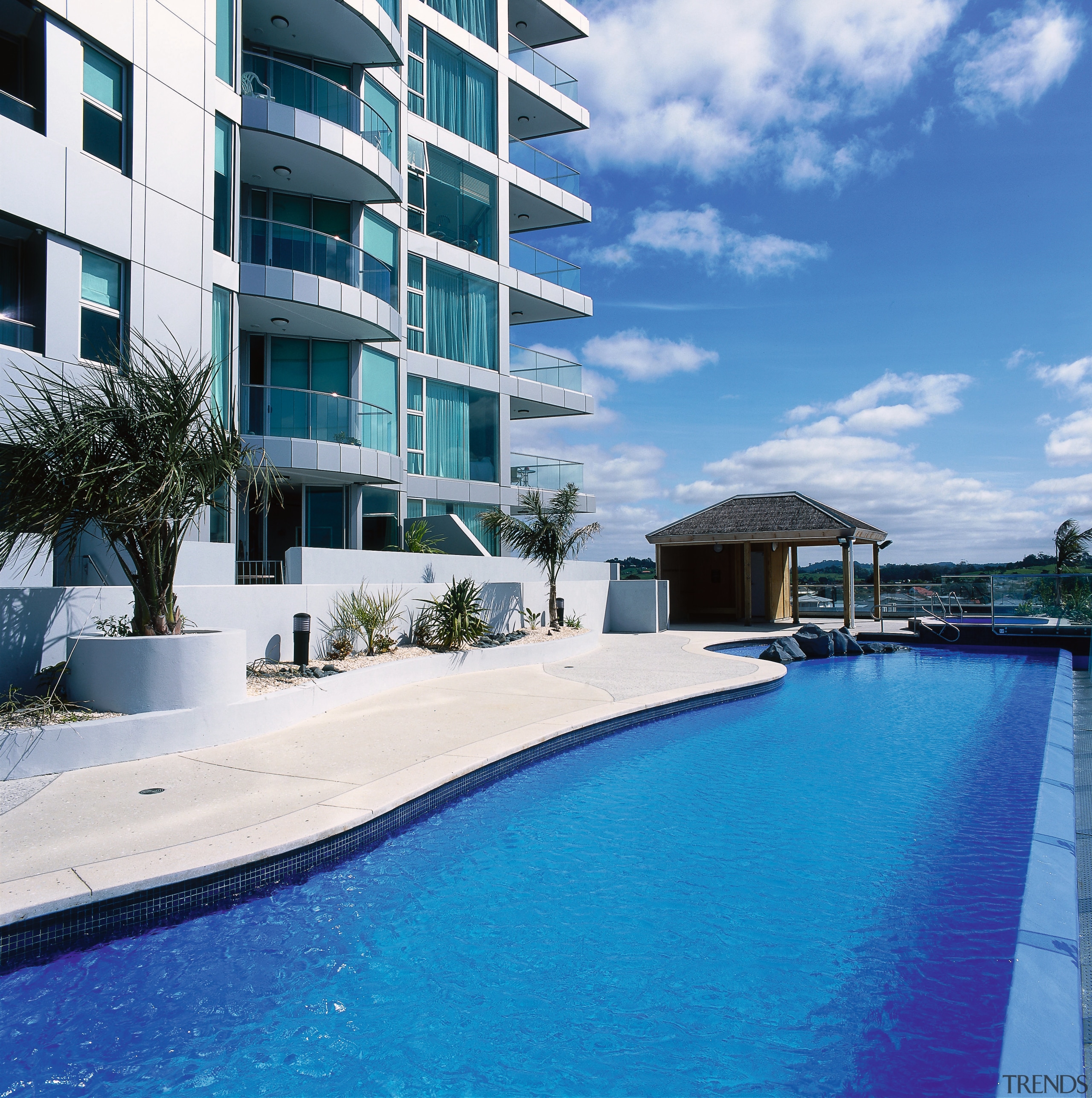 Curved edge pool in front of apartment building, apartment, building, condominium, estate, hotel, house, leisure, property, real estate, residential area, resort, sky, swimming pool, vacation, water, teal, white