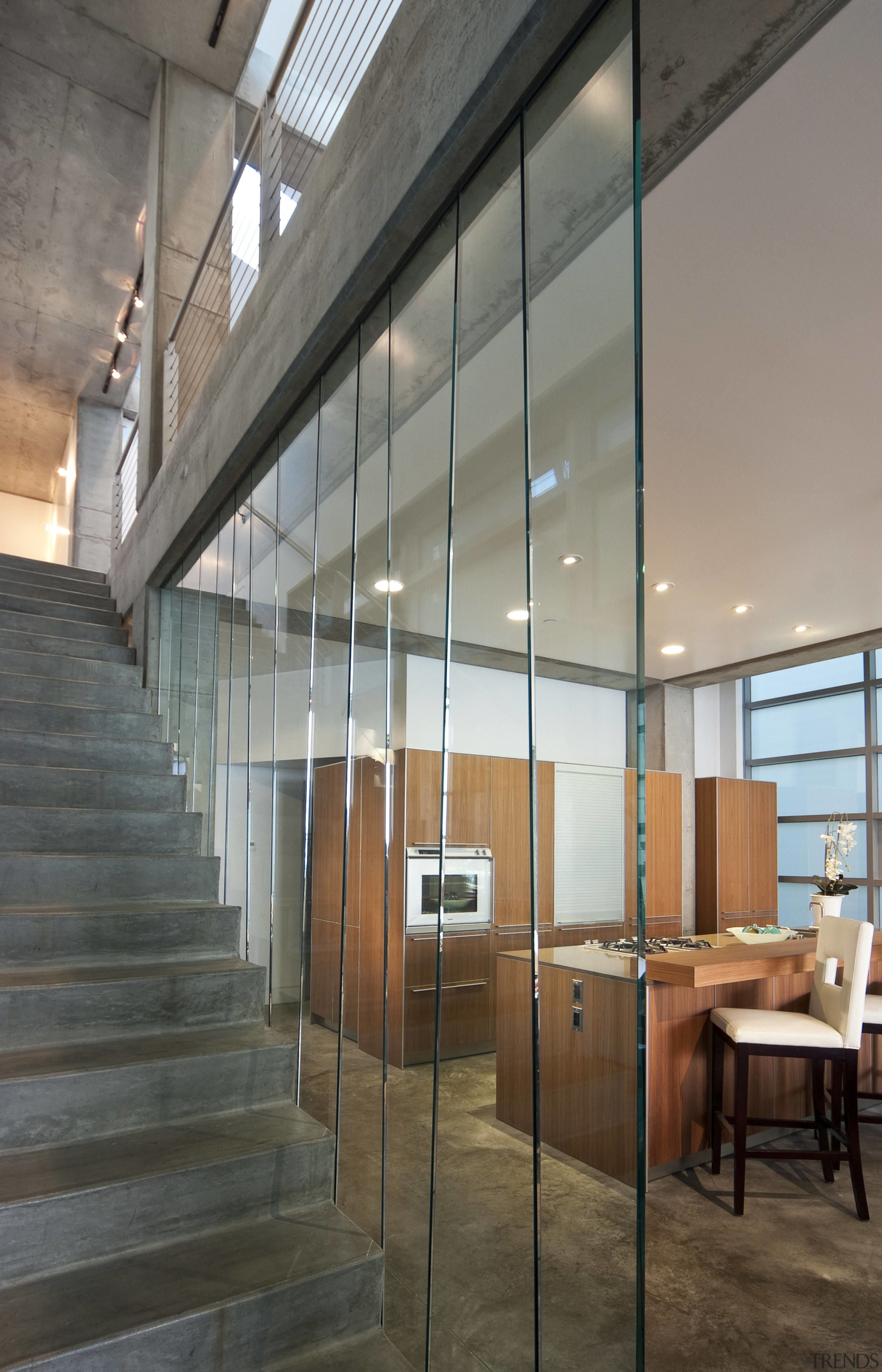 View of kitchen from stairwell featuring concrete floors, architecture, ceiling, daylighting, floor, glass, interior design, loft, wall, gray