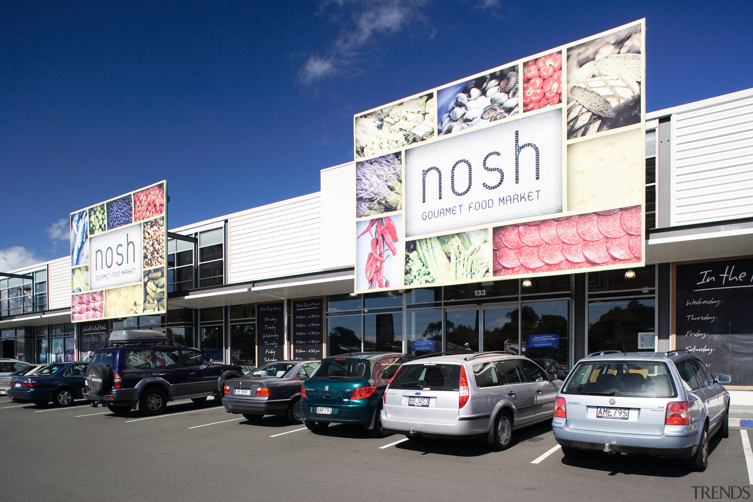 A view of this block of retail premises advertising, billboard, building, car, city, compact car, downtown, family car, luxury vehicle, real estate, sedan, signage, vehicle, blue, white