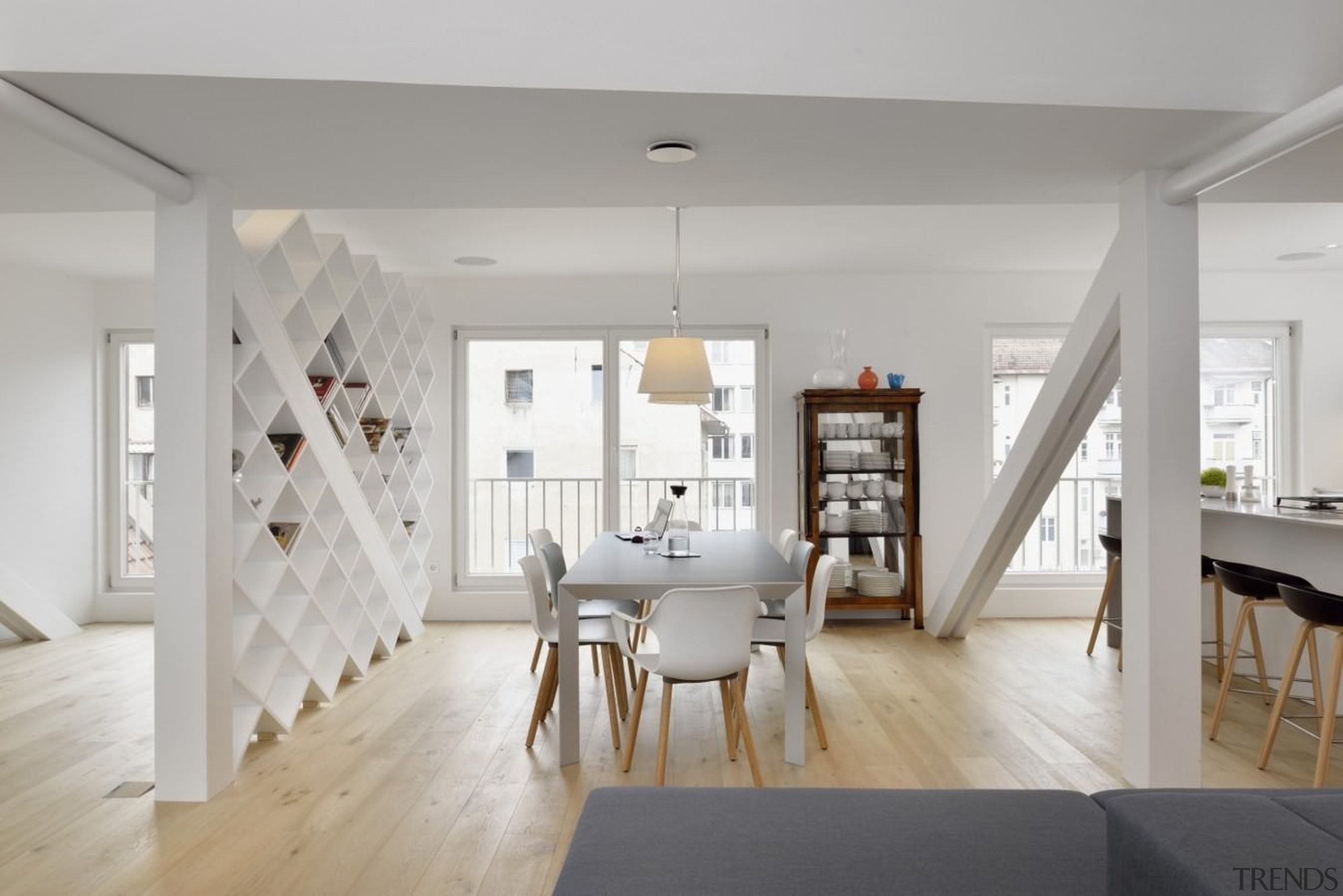 The dining room sits between two building support architecture, ceiling, dining room, floor, flooring, home, house, interior design, interior designer, living room, loft, room, table, wall, wood flooring, gray