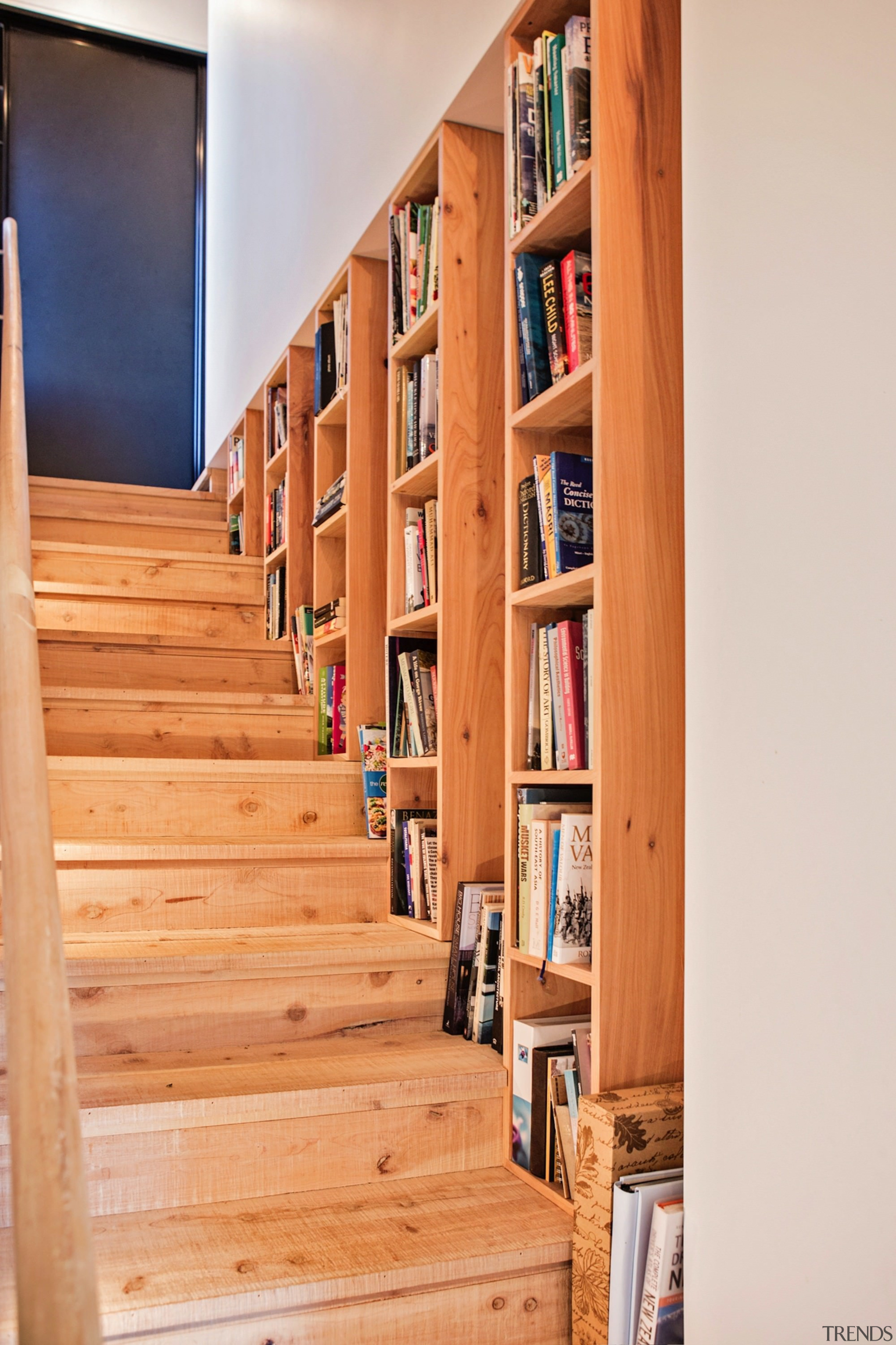 A bookshelf integrated into the stairway wall - bookcase, floor, flooring, furniture, hardwood, home, shelf, shelving, stairs, wood, orange, white