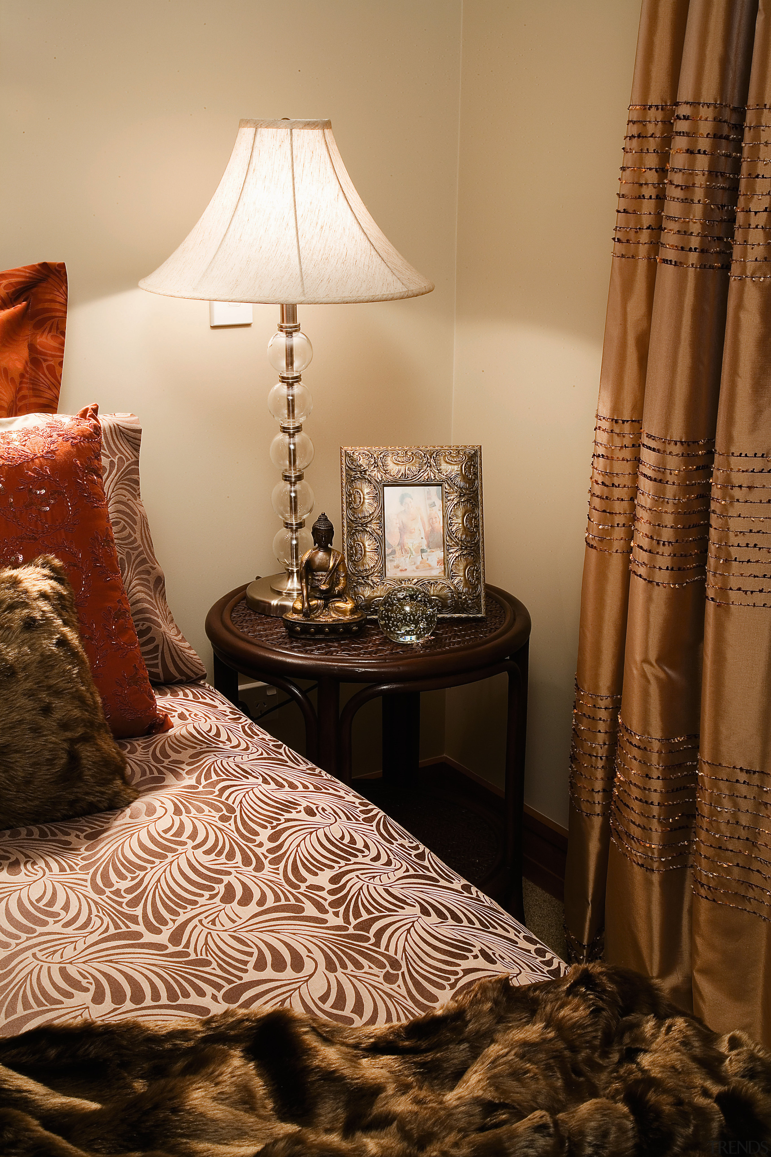 Bedroom with patterned bedding, cushions and throw, small bed, bed frame, bedroom, curtain, flooring, furniture, home, interior design, lampshade, light fixture, lighting, lighting accessory, living room, room, table, textile, window, window treatment, brown, orange