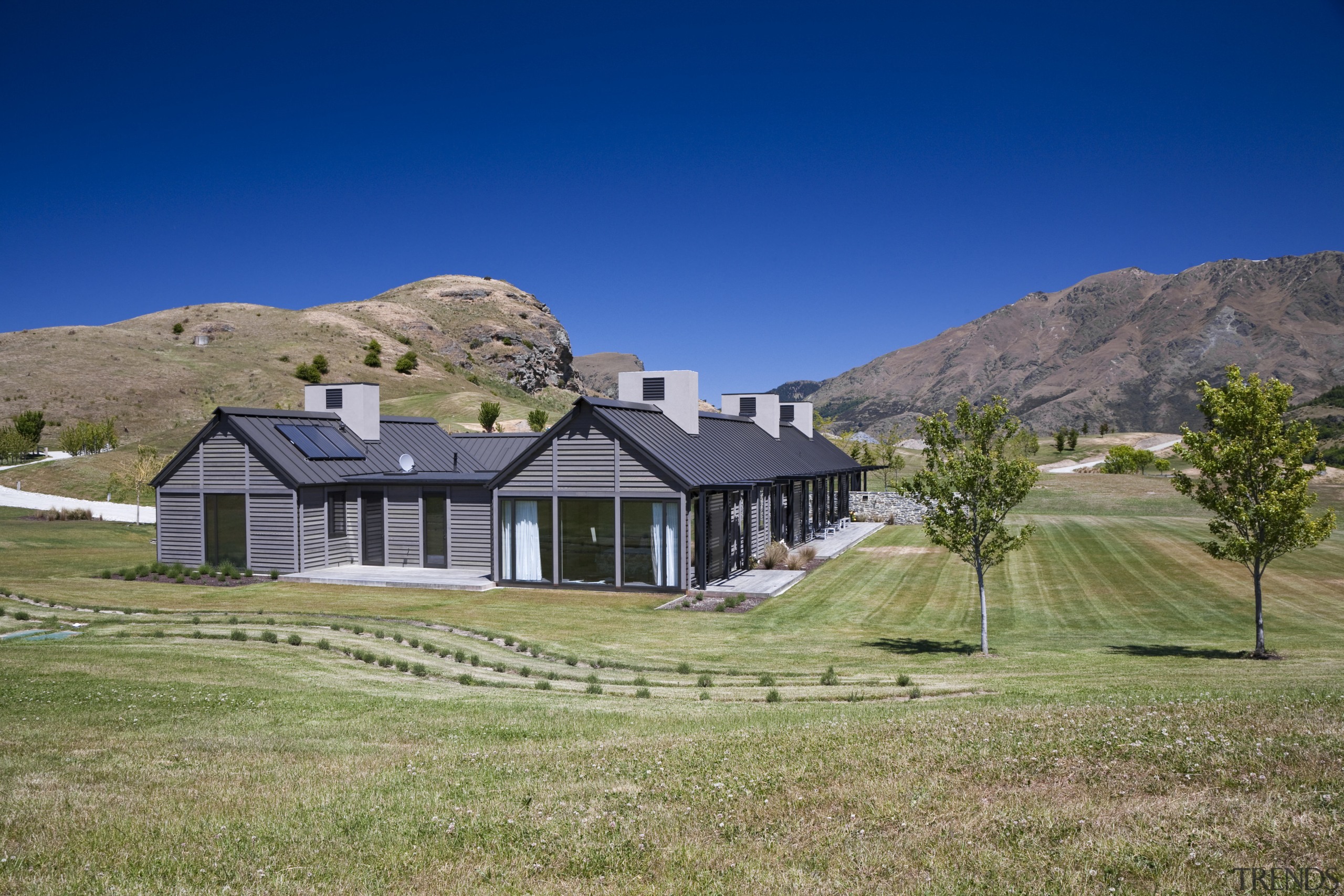 Exterior view of a country home which features alps, cottage, elevation, estate, farm, farmhouse, field, grass, grassland, highland, hill, home, house, land lot, landscape, meadow, mountain, mountain range, property, real estate, residential area, rural area, sky, suburb, tree, villa, blue, brown