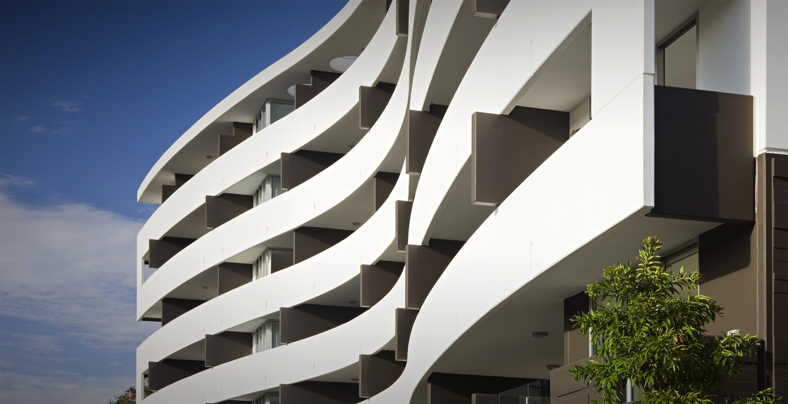 Exterior view of the Flow Apartments which sit apartment, architecture, building, commercial building, condominium, corporate headquarters, daylighting, facade, headquarters, mixed use, real estate, sky, structure, white