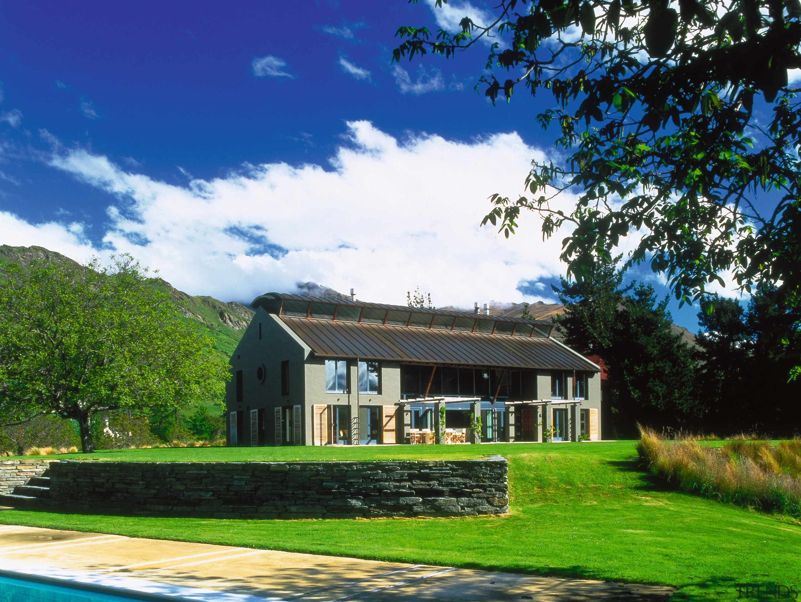 An exterior view of this rural home designed cottage, estate, facade, farm, farmhouse, grass, home, house, land lot, landscape, lawn, plantation, property, real estate, roof, sky, tree, villa