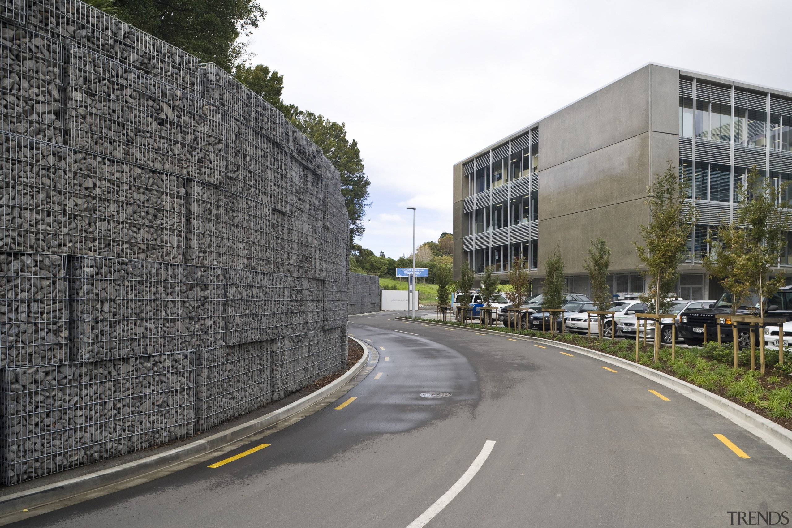 View of a large retaining wall with a architecture, asphalt, building, car, city, infrastructure, lane, metropolitan area, neighbourhood, residential area, road, road surface, sky, street, tree, wall, gray
