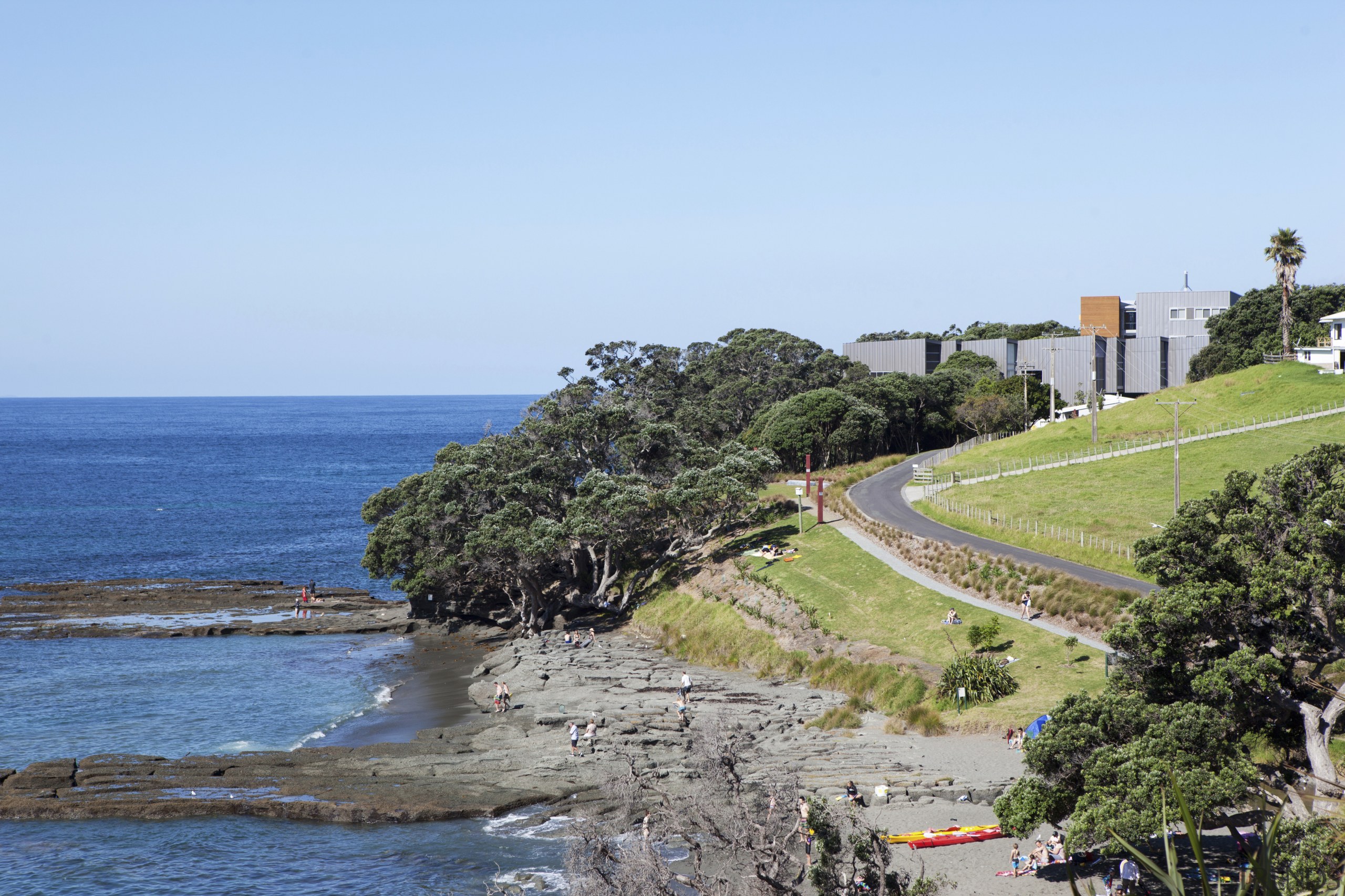 View of path from buildings to sea. - bay, beach, body of water, coast, coastal and oceanic landforms, headland, ocean, plant, promontory, sea, shore, sky, terrain, tree, teal