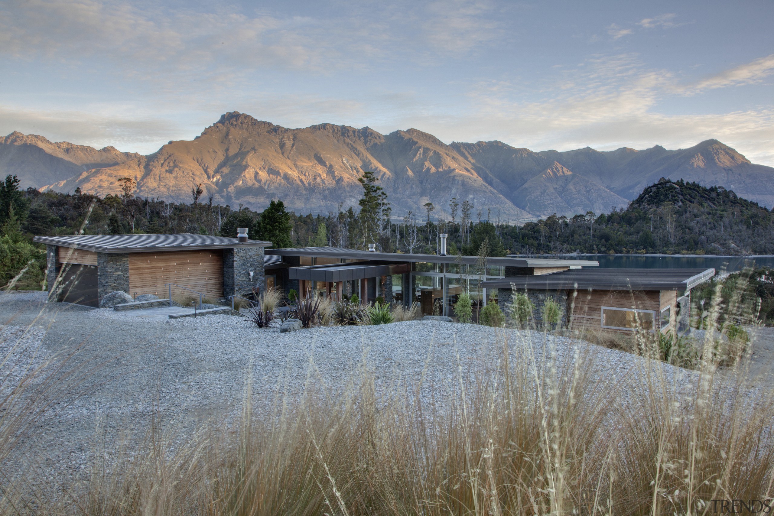 This house achieves privacy from the street by home, house, lake, landscape, mountain, mountain range, mountainous landforms, property, real estate, reflection, sky, tree, water, wilderness, winter, gray