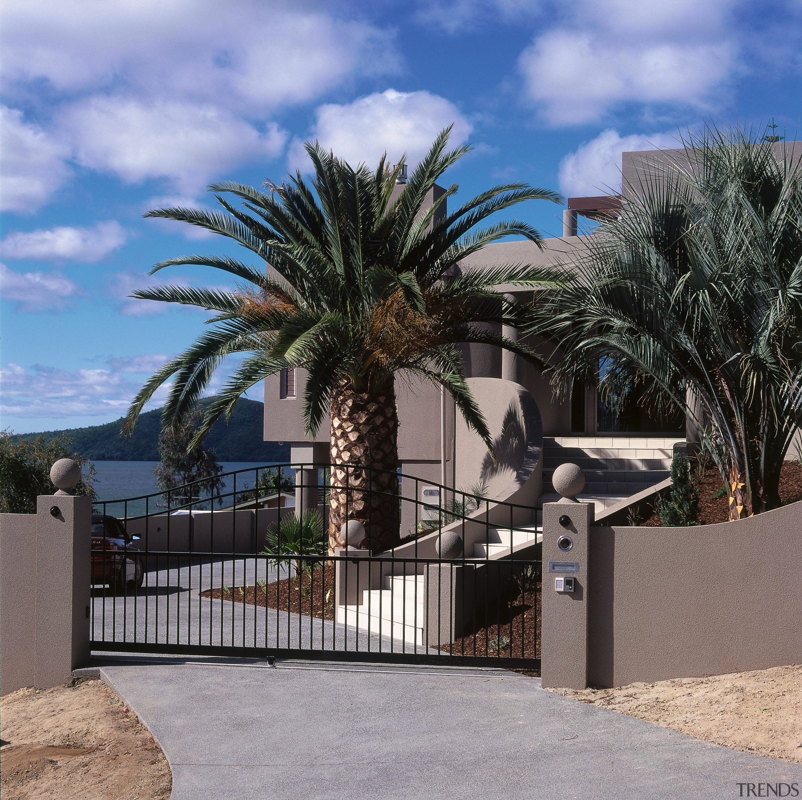 A view of this new lake front house architecture, arecales, estate, fence, home, outdoor structure, palm tree, plant, property, real estate, residential area, sky, tree, wall, black, gray