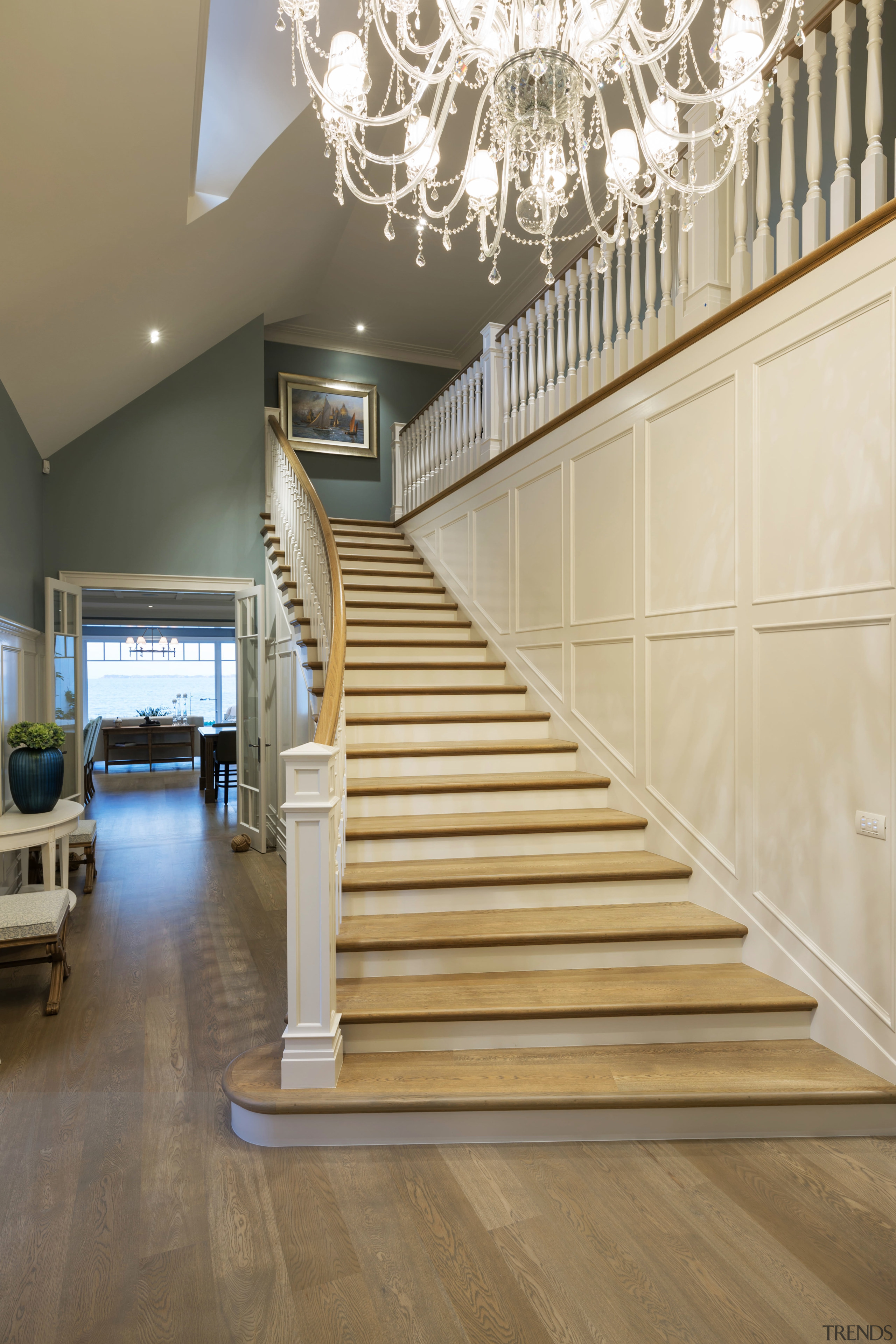 A splayed, ornate staircase with traditional chandelier overhead baluster, ceiling, daylighting, floor, flooring, handrail, hardwood, interior design, laminate flooring, lobby, stairs, wall, wood, wood flooring, orange, brown