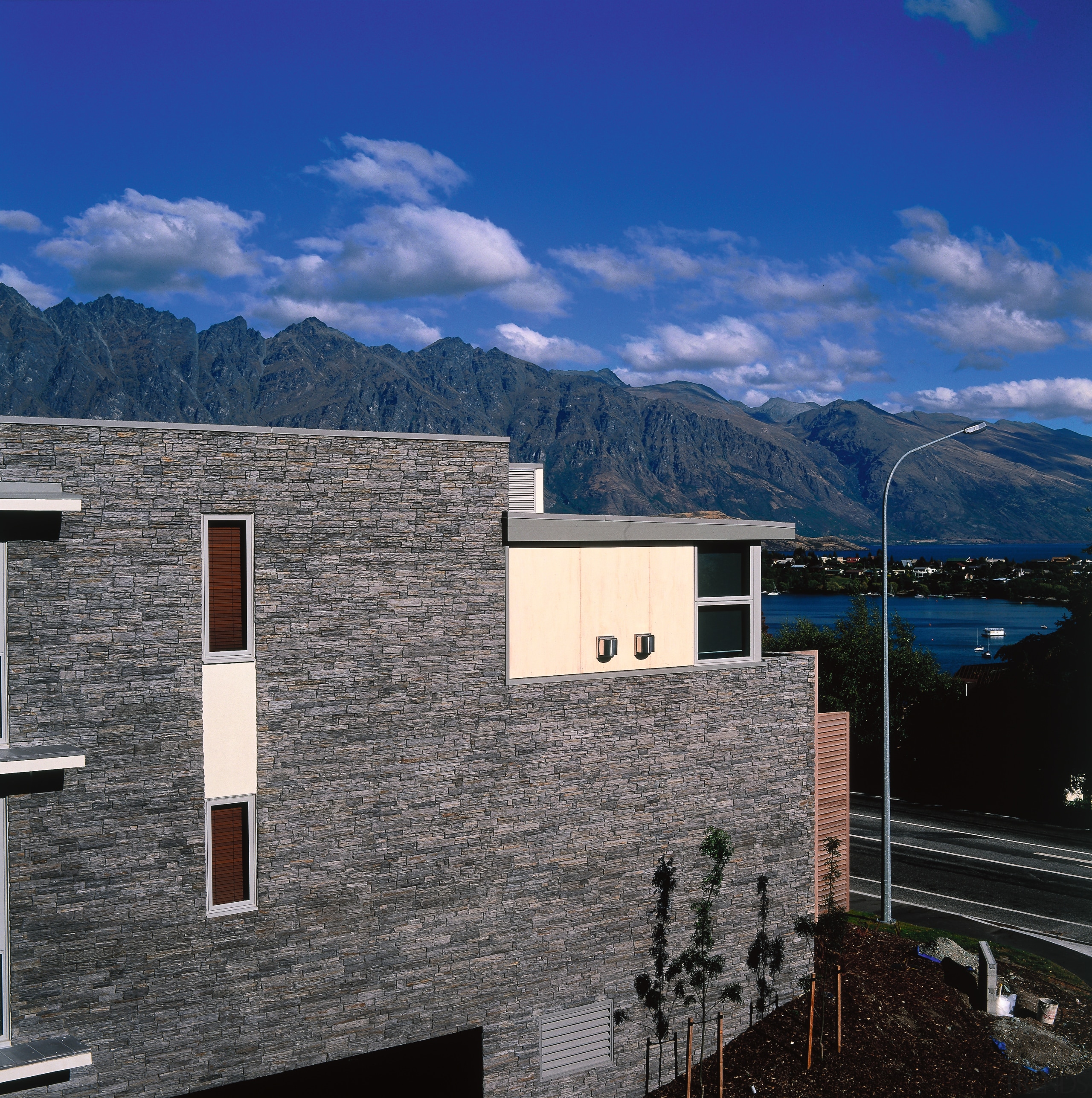 Exterior view of apartment showing stone cladding with architecture, building, cloud, elevation, facade, home, house, mountain, mountain range, property, real estate, residential area, roof, sky, window, blue, black