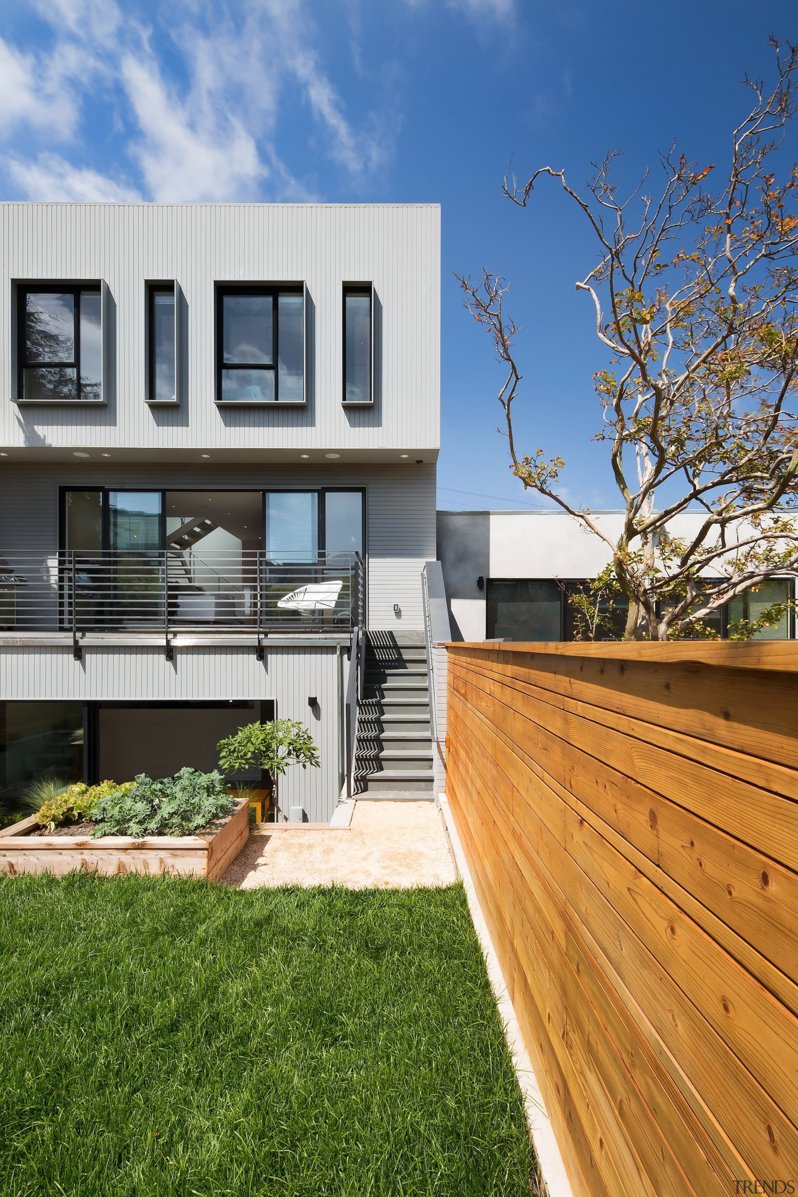 A timber boundary fence contrasts with the home apartment, architecture, backyard, balcony, deck, estate, facade, grass, home, house, neighbourhood, outdoor structure, property, real estate, residential area, siding, wood, yard