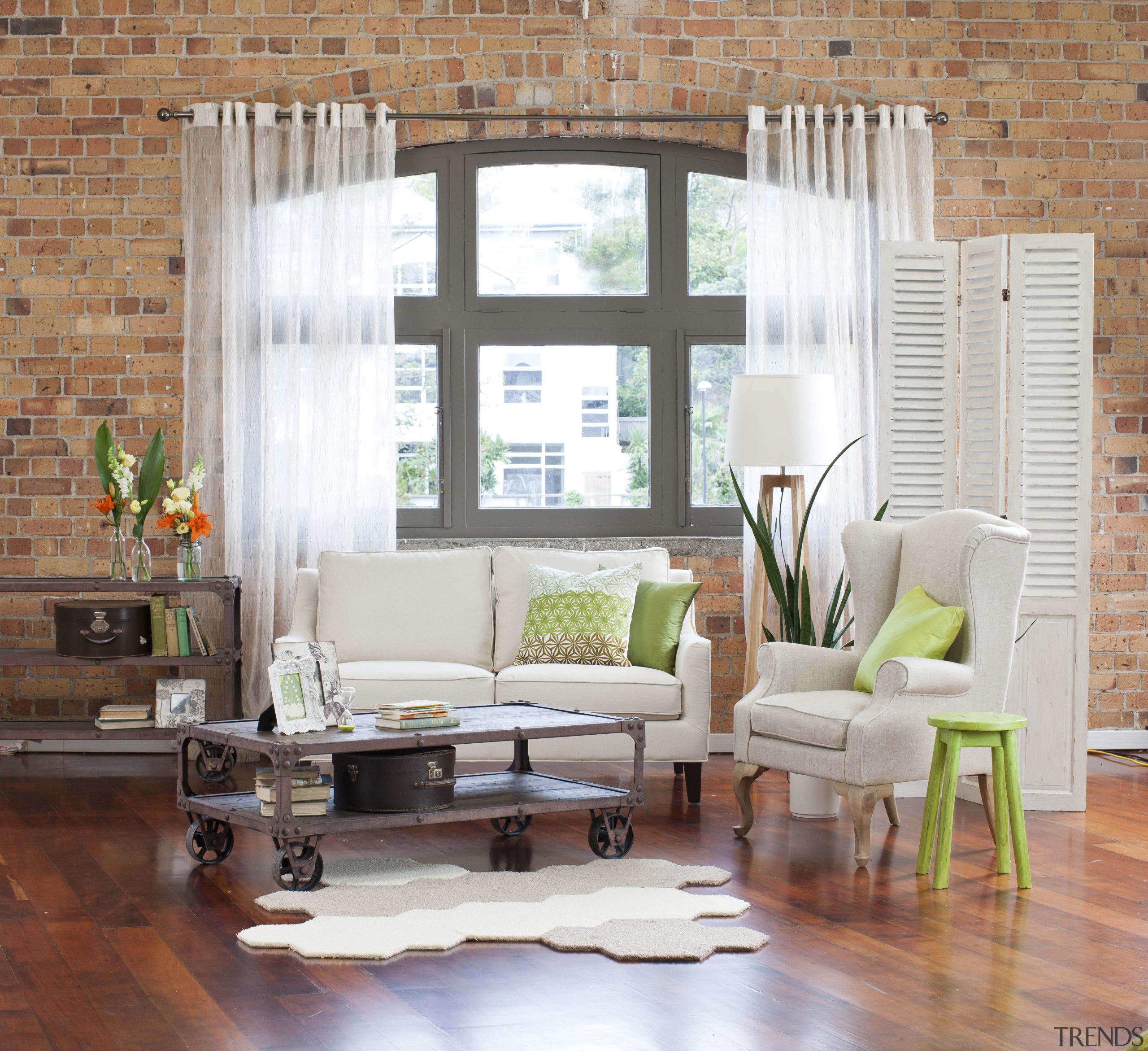 Living room with wooden flooring and brick wall. chair, curtain, floor, furniture, hardwood, home, interior design, living room, room, table, wall, window, window blind, window covering, window treatment, wood, wood flooring, gray