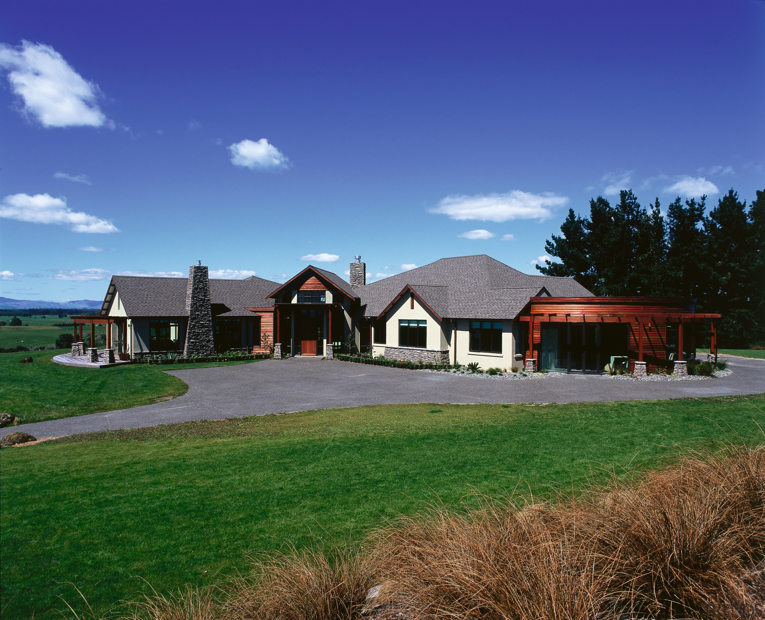 A photograph of a rural house. The house cloud, cottage, estate, farm, farmhouse, grass, home, house, land lot, landscape, property, real estate, residential area, roof, rural area, siding, sky, suburb, blue