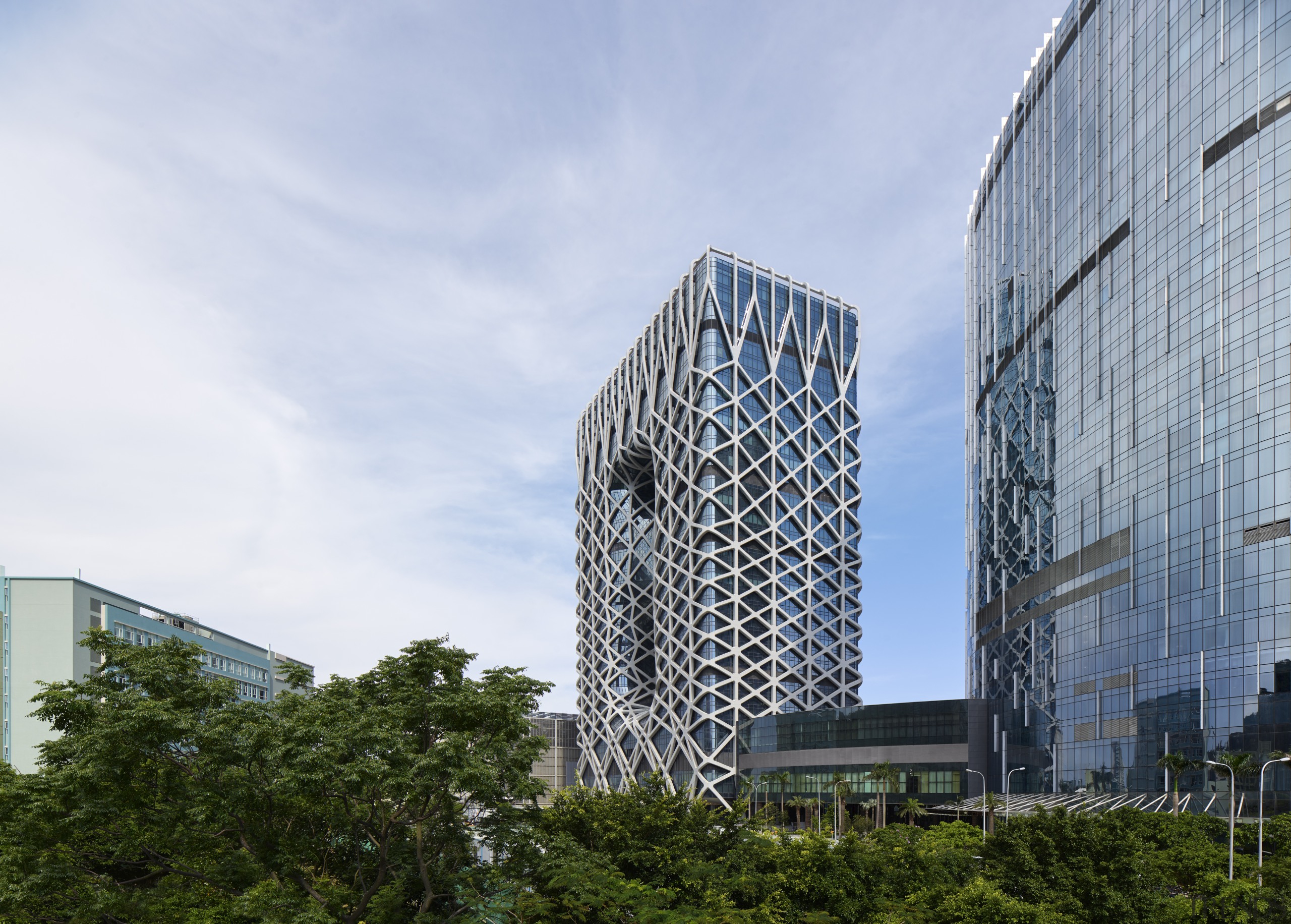 The glazed facade behind Morpheus Hotel’s exoskeleton comprises architecture, building, city, condominium, corporate headquarters, daytime, facade, headquarters, metropolis, metropolitan area, mixed use, residential area, sky, skyscraper, tower block, tree, urban area, white