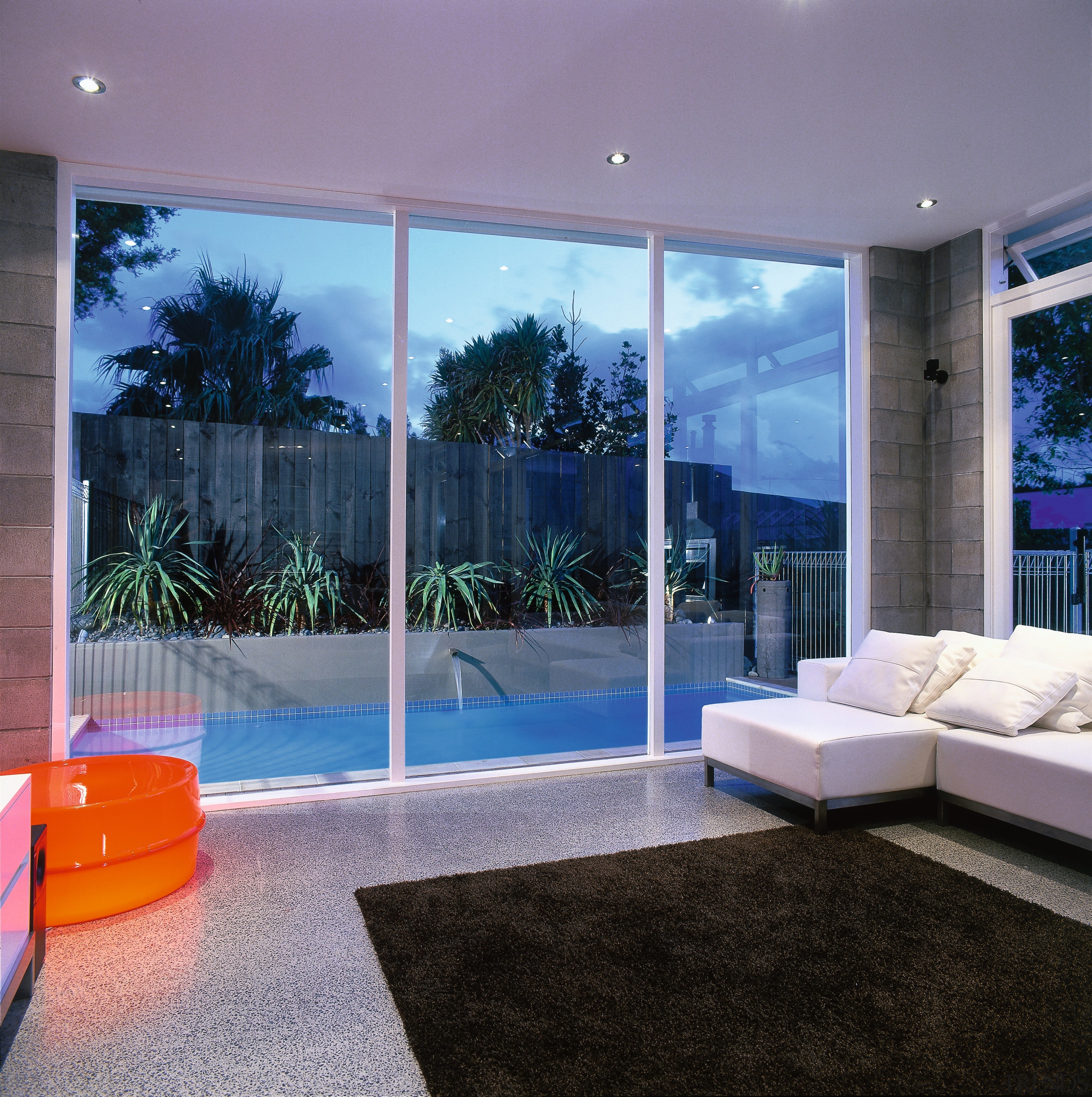 Living area with brown rug, white sofa, concrete door, glass, home, interior design, living room, property, real estate, wall, window, purple