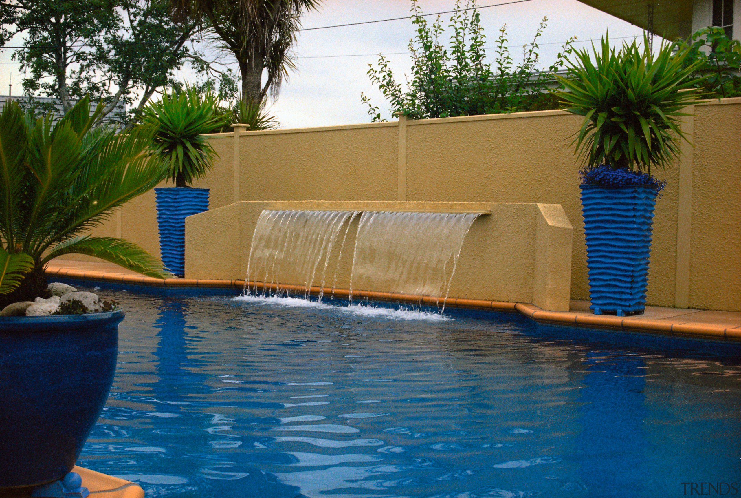 Blue outdoor pool with waterfall feature, tan coloured arecales, backyard, leisure, majorelle blue, palm tree, plant, property, real estate, resort, swimming pool, tree, water, water feature, brown