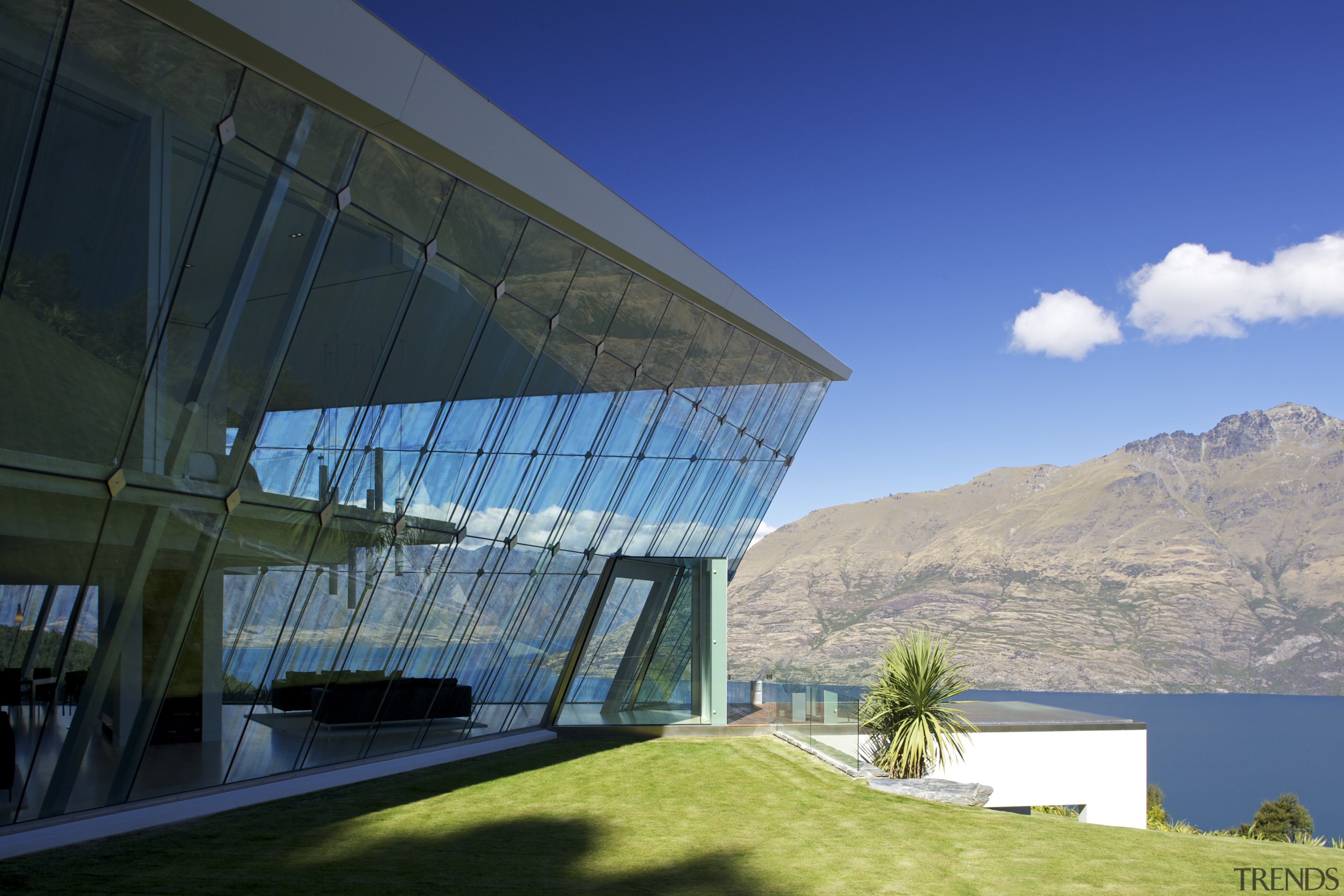 This glass-walled house appears to emerge directly from architecture, building, corporate headquarters, daylighting, elevation, estate, facade, headquarters, home, house, mountain range, property, real estate, roof, sky, blue, black