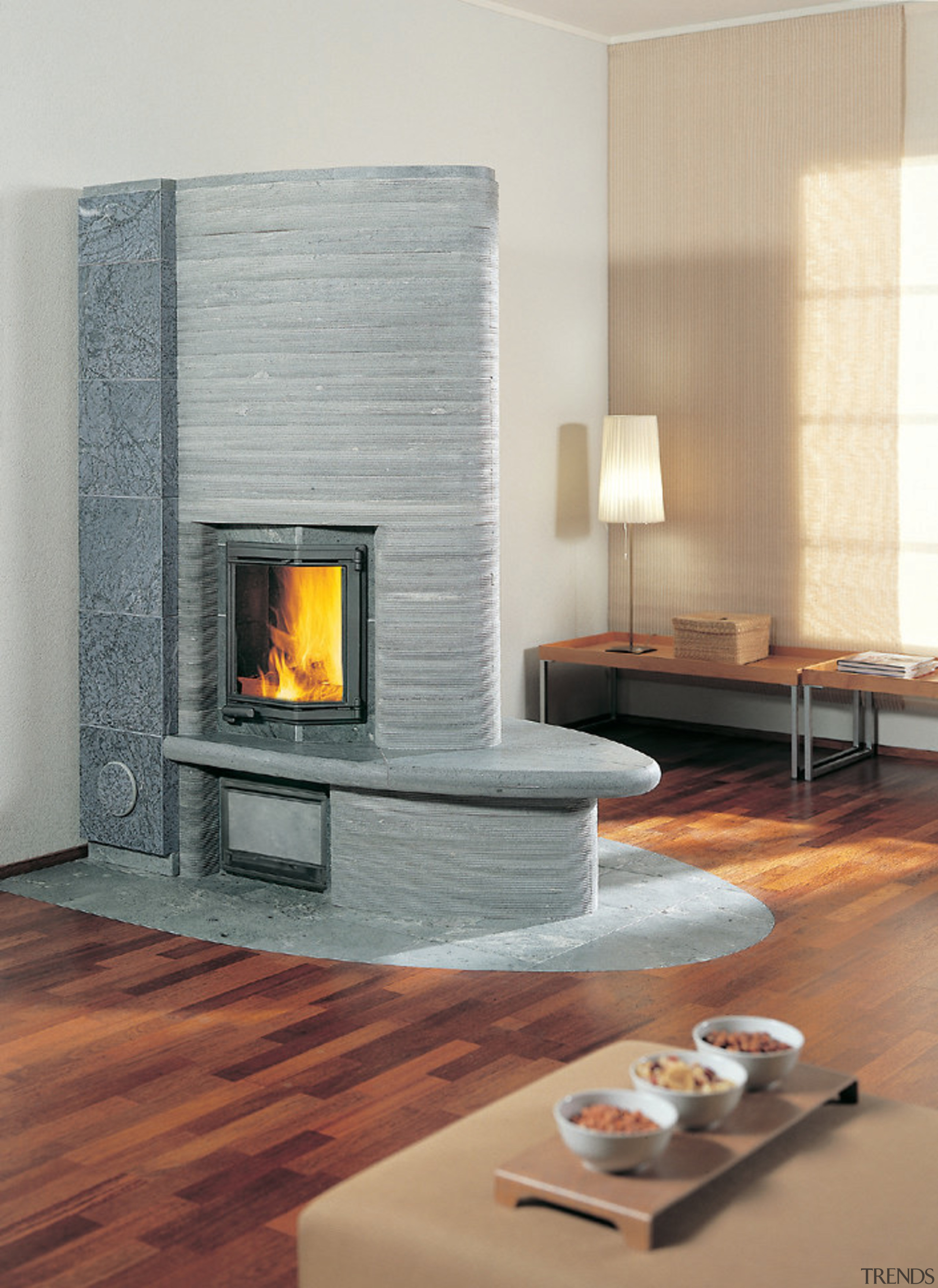 A photograph of a curved fireplace. The area fireplace, floor, flooring, hearth, heat, home appliance, wood burning stove, gray