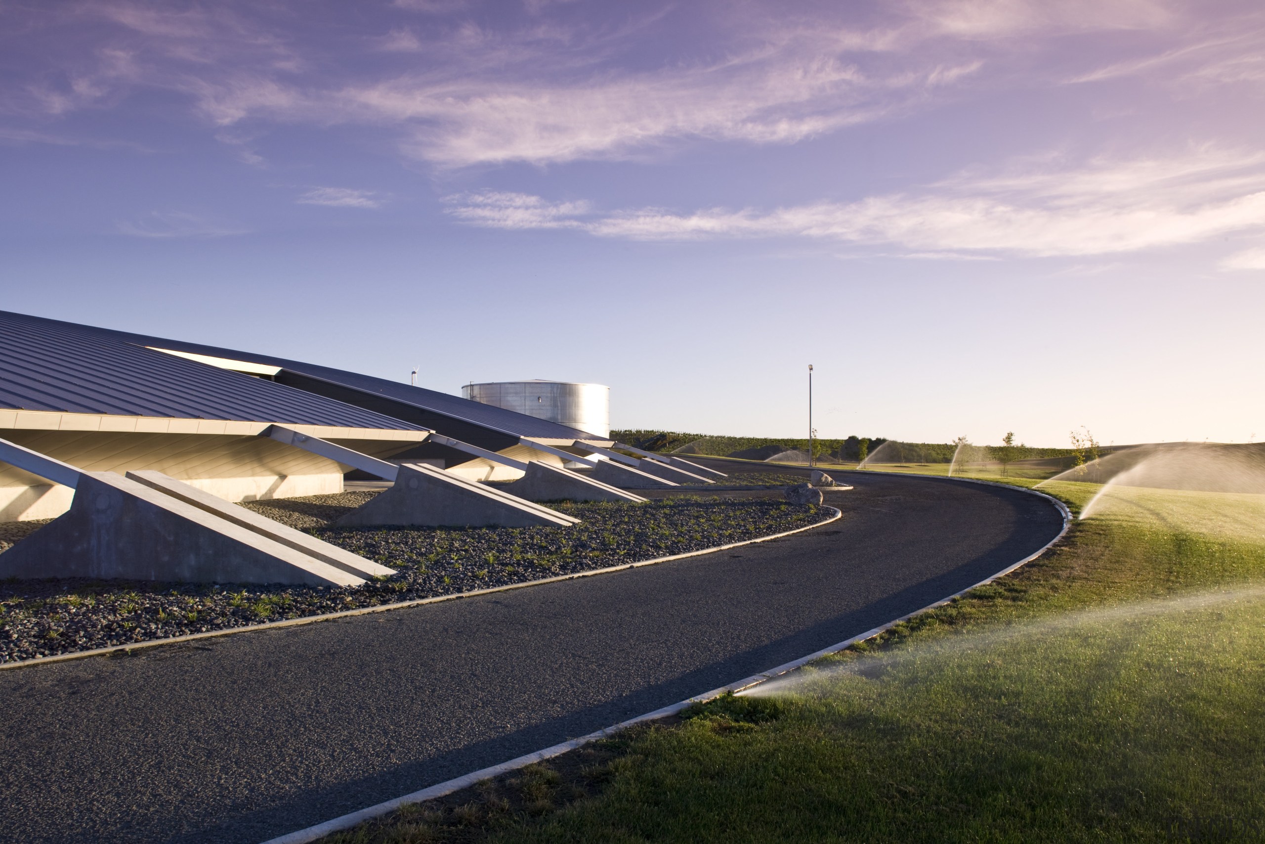 Exterior view of the sustainable production building which architecture, asphalt, atmosphere of earth, cloud, energy, field, fixed link, grass, highway, horizon, infrastructure, line, residential area, road, road surface, sky, structure, sunlight, purple