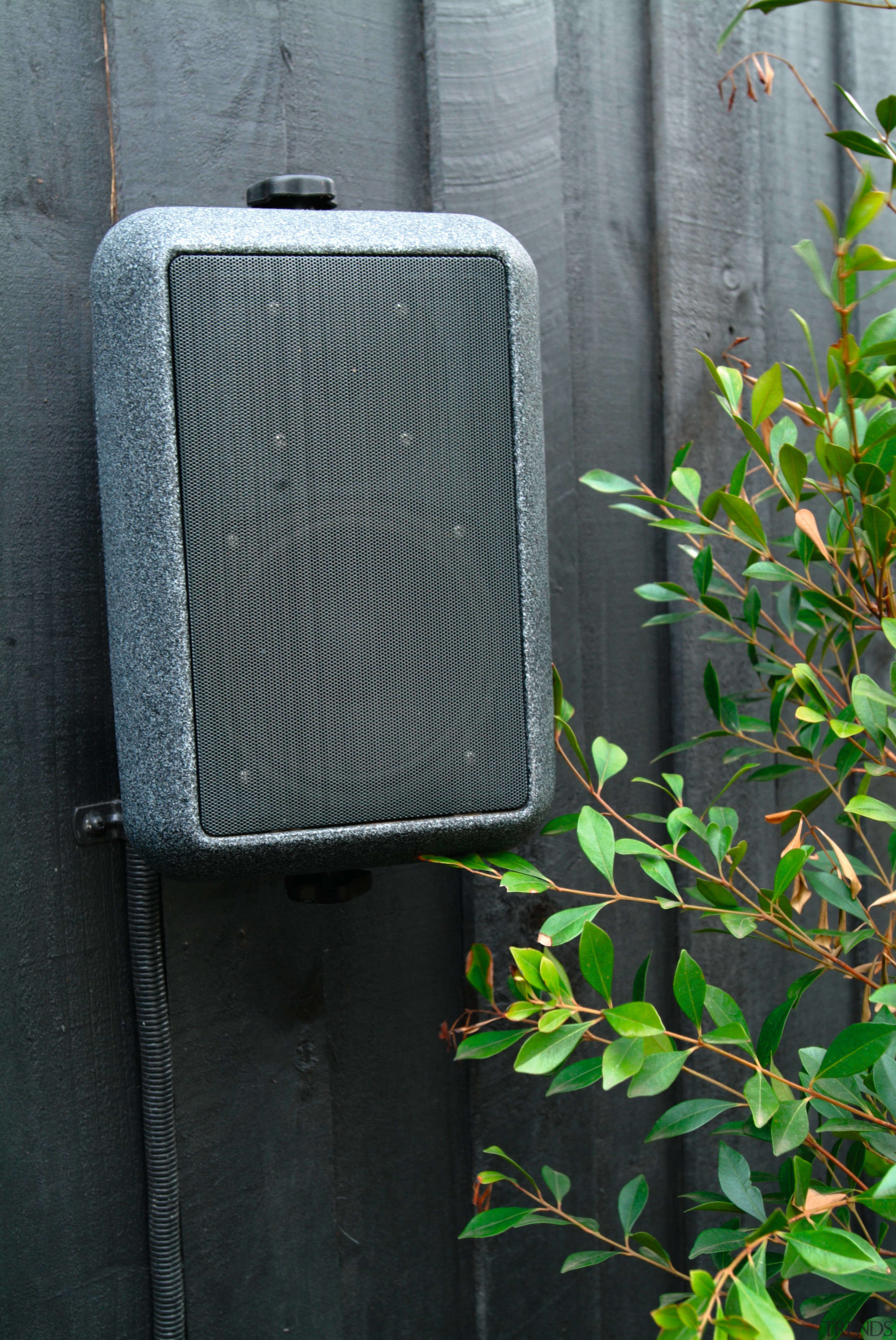 view of the outdoor speaker mounted to the grass, wall, black, gray