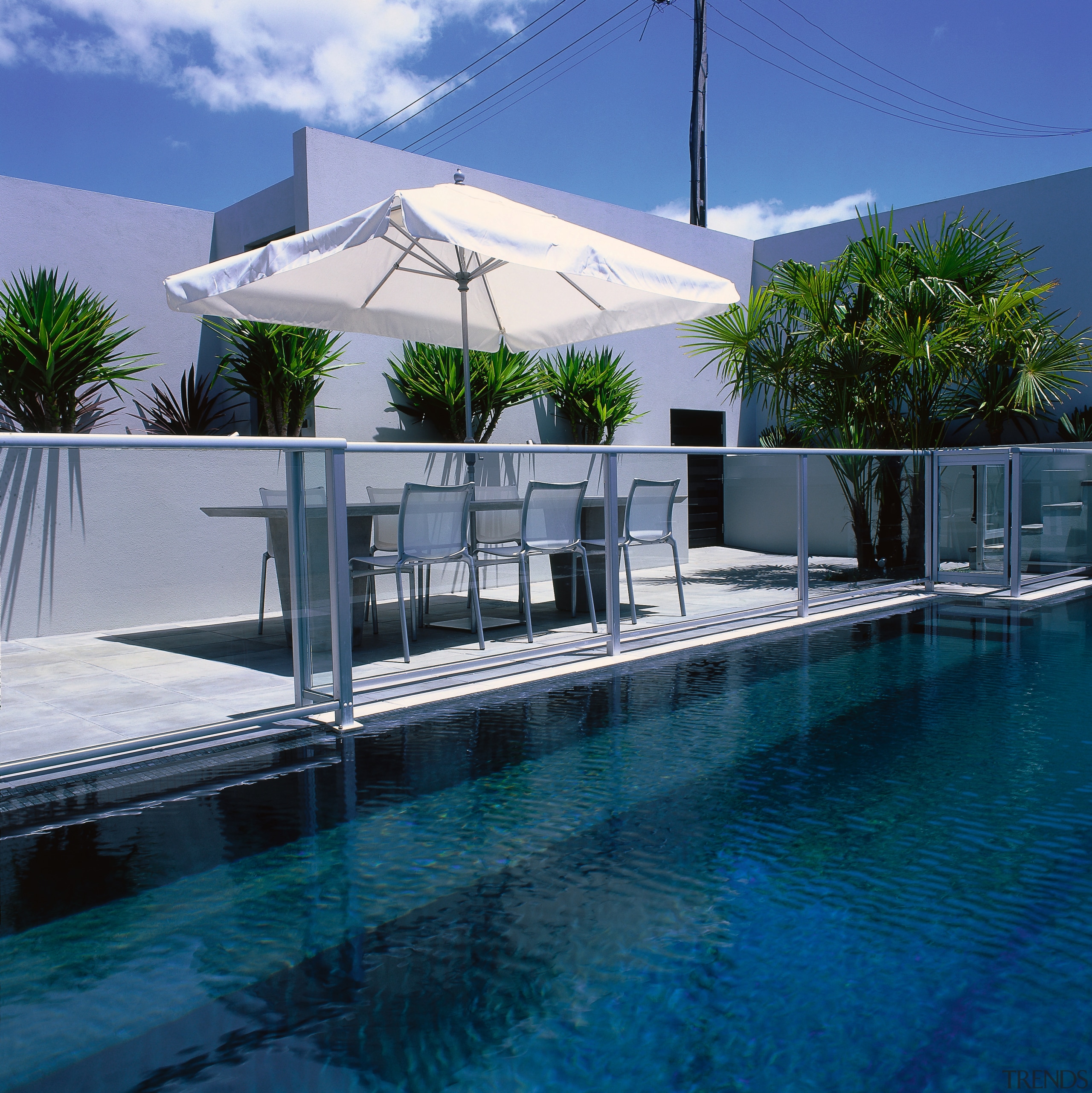 Blue pool with grey paved patio area, glass architecture, condominium, estate, house, leisure, property, real estate, resort, shade, swimming pool, villa, water, blue, teal