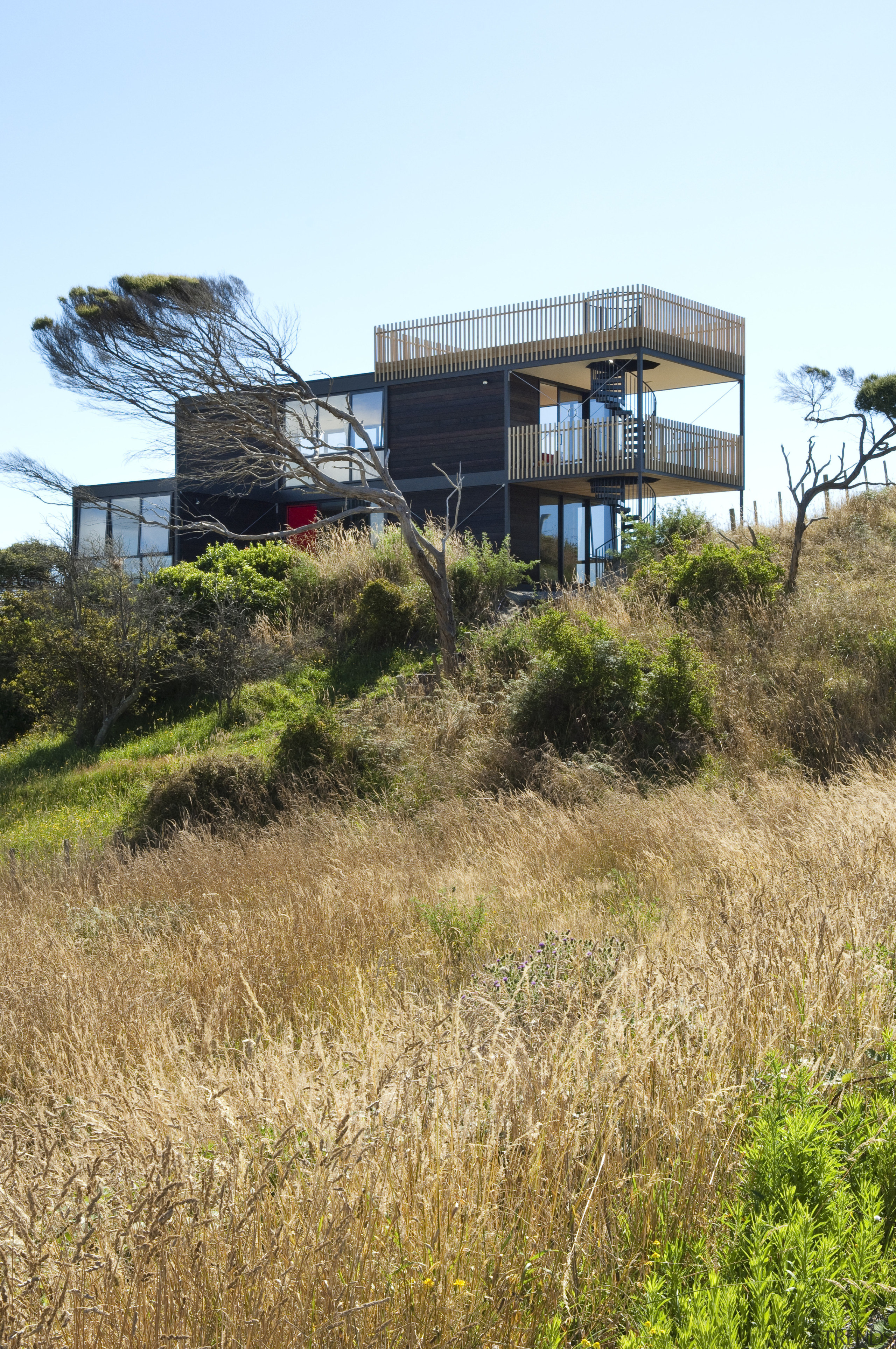 View of multilevel home on tussocky slope. - architecture, building, cottage, grass, home, house, land lot, property, real estate, sky, brown, white