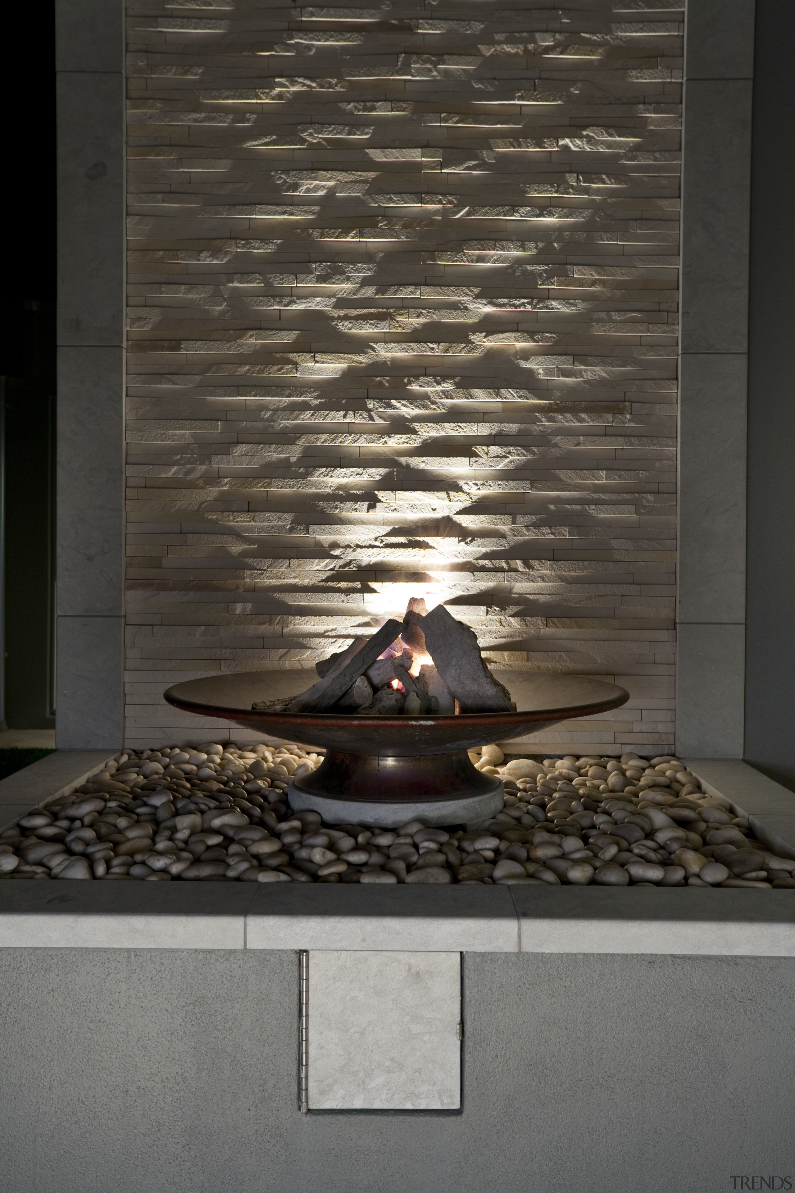 View of sleek poolscape with textured stone wall, floor, flooring, hearth, wall, black, gray