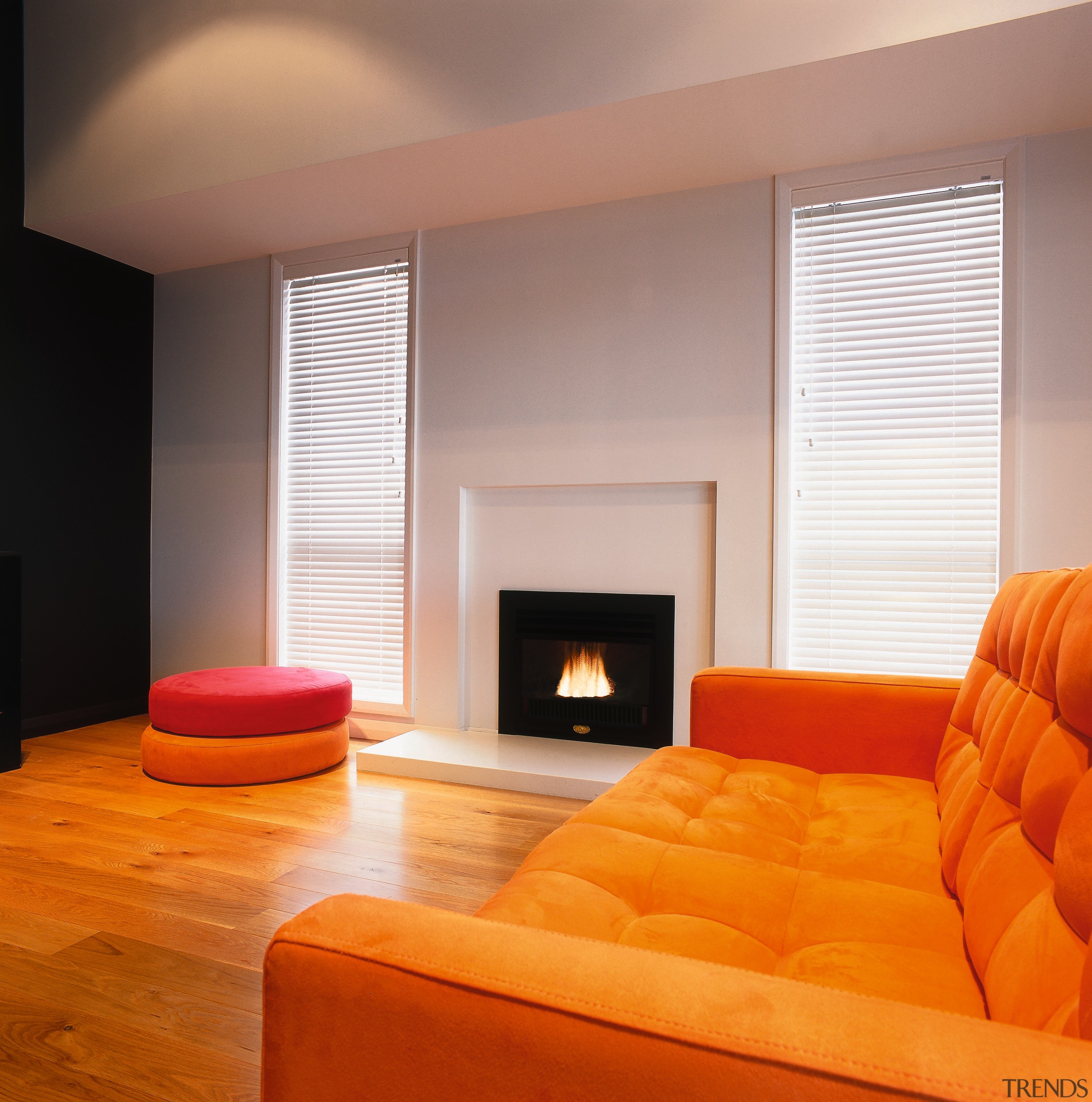 Fireplace set into white wall in lounge with architecture, ceiling, couch, fireplace, floor, flooring, hardwood, hearth, home, interior design, living room, orange, room, window, window covering, window treatment, wood, wood flooring, orange, gray