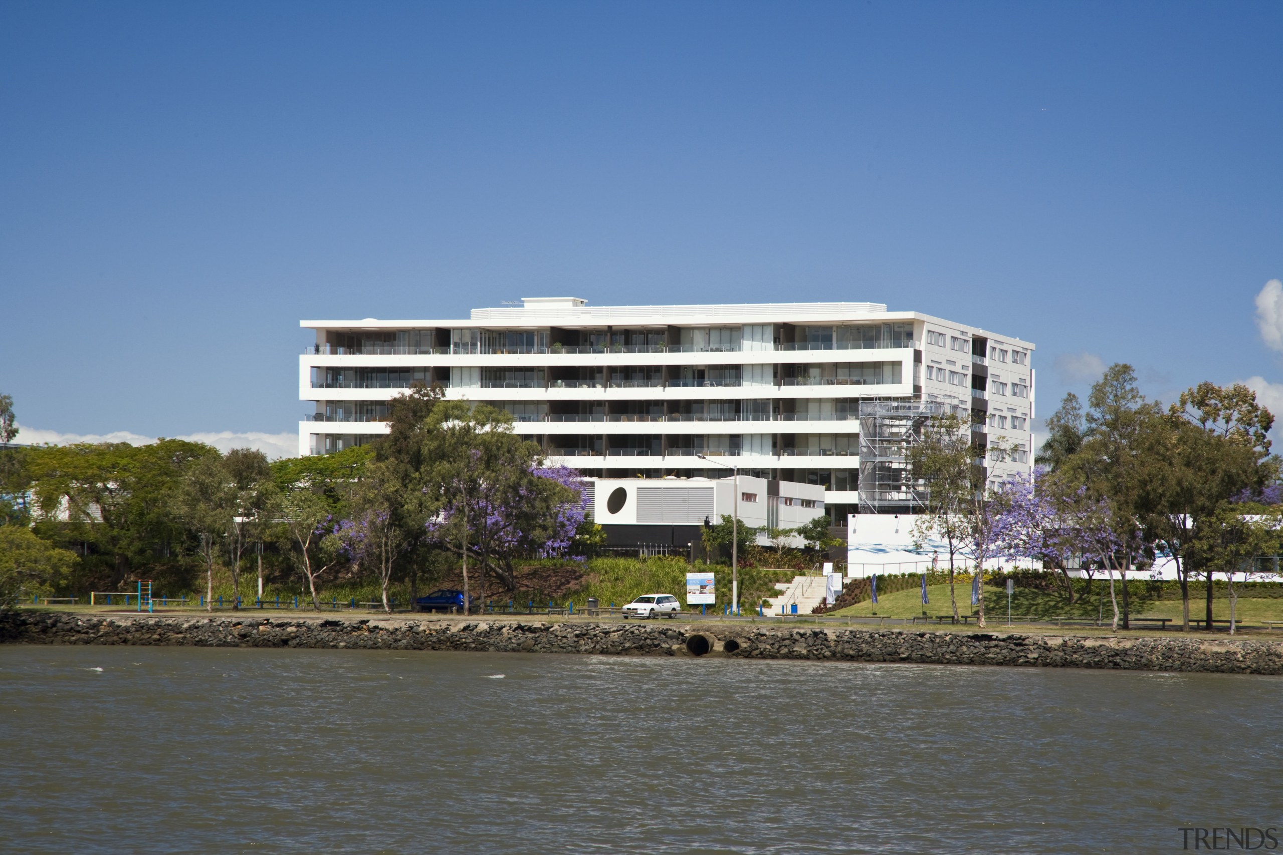 Image of a development which is part of apartment, architecture, building, canal, city, condominium, corporate headquarters, daytime, estate, facade, headquarters, home, house, mixed use, real estate, reflection, residential area, river, sky, tower block, tree, water, waterway, teal