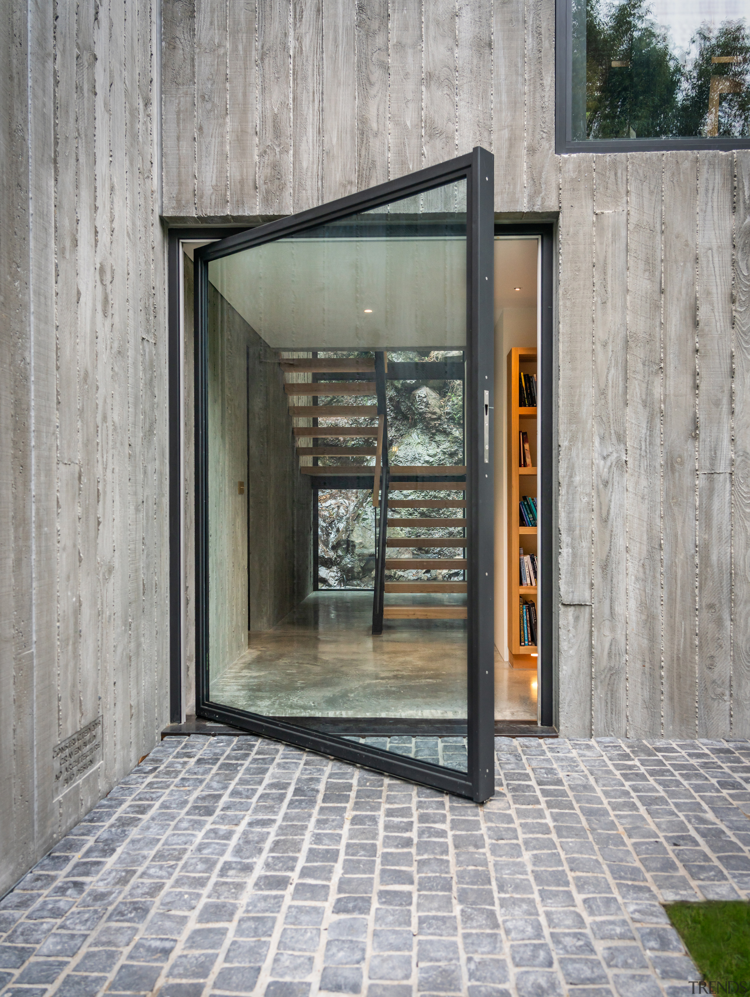 A black-framed pivot door opens to the home's 