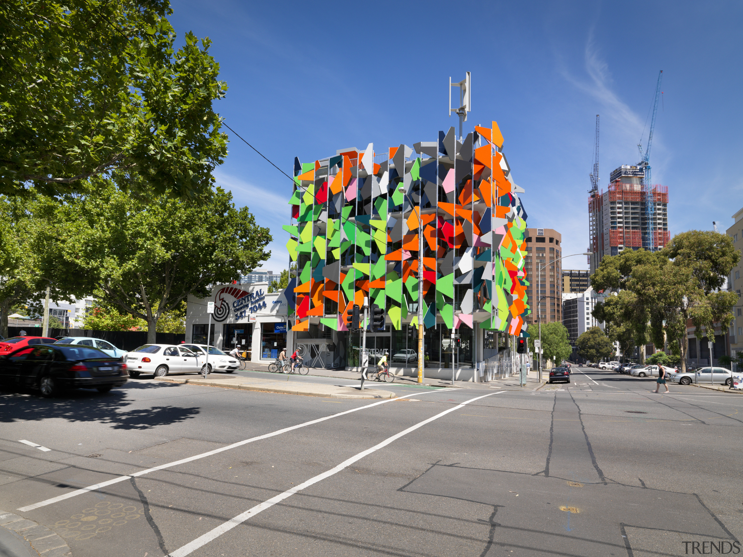 View of Pixel Building, with colorful exterior flags, car, city, downtown, landmark, metropolis, metropolitan area, mixed use, neighbourhood, pedestrian, road, sky, street, tourist attraction, town square, tree, urban area, gray