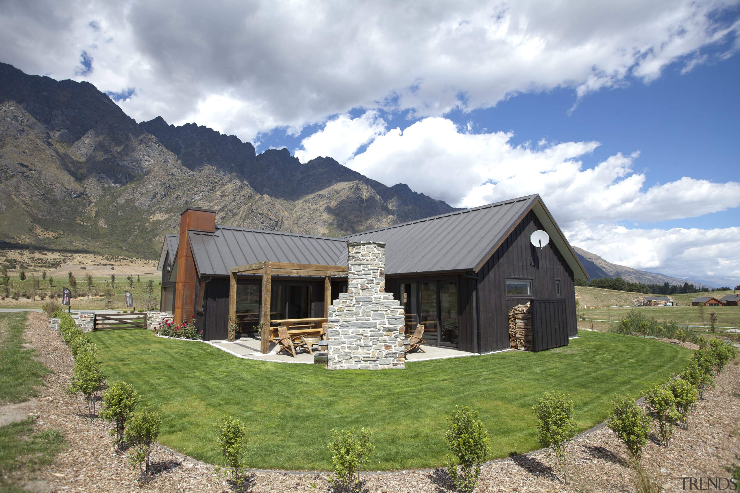 Exterior view of house with rounded lawn, stone barn, cloud, cottage, elevation, estate, farmhouse, home, house, hut, landscape, log cabin, mountain, mountain range, property, real estate, rural area, sky, gray