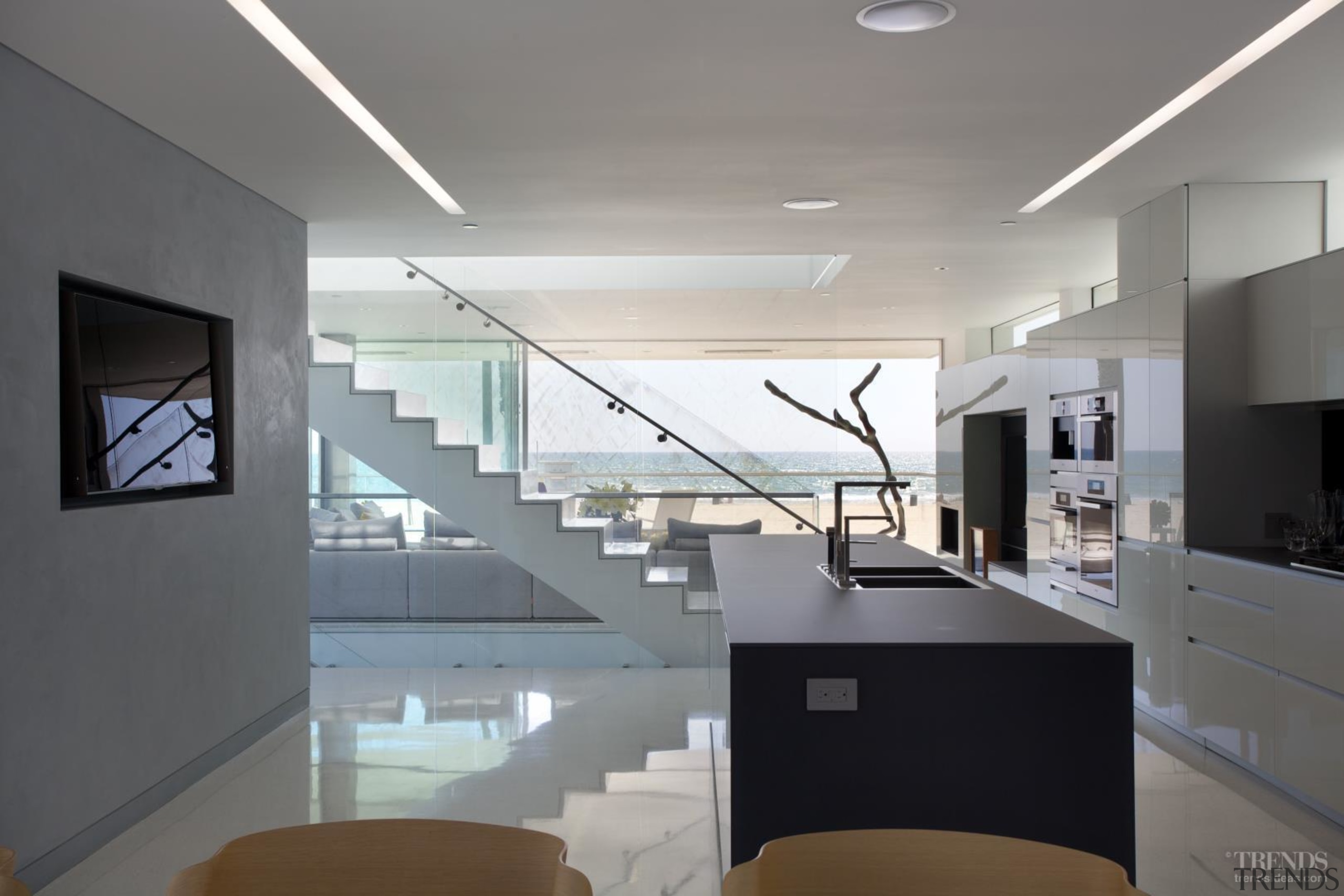 Backpainted glass cabinets in this galley-style kitchen reflect architecture, ceiling, daylighting, glass, handrail, house, interior design, kitchen, gray