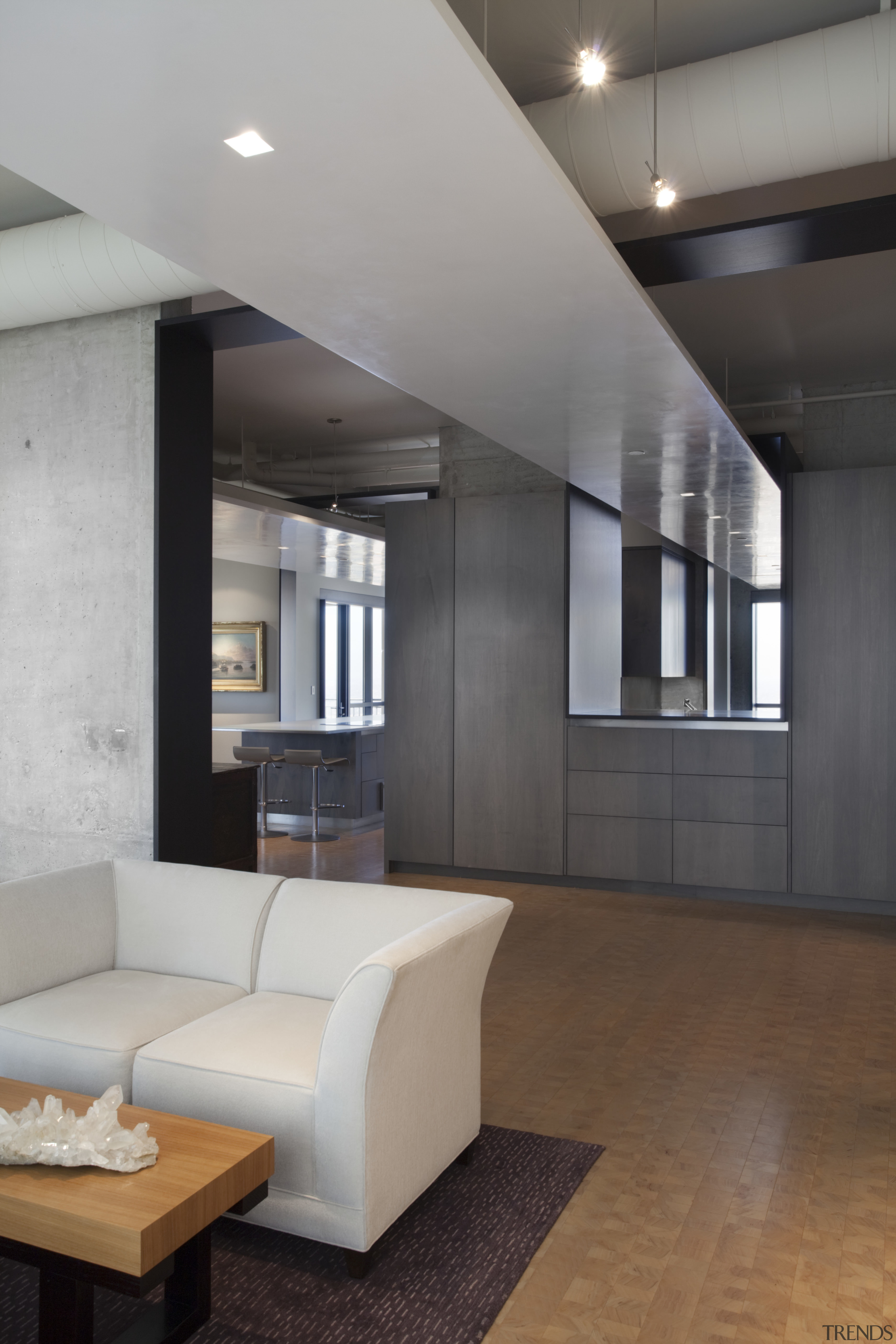 View of an apartment kitchen with dark-toned cabinetry, architecture, ceiling, floor, flooring, interior design, laminate flooring, living room, lobby, loft, wall, wood flooring, gray