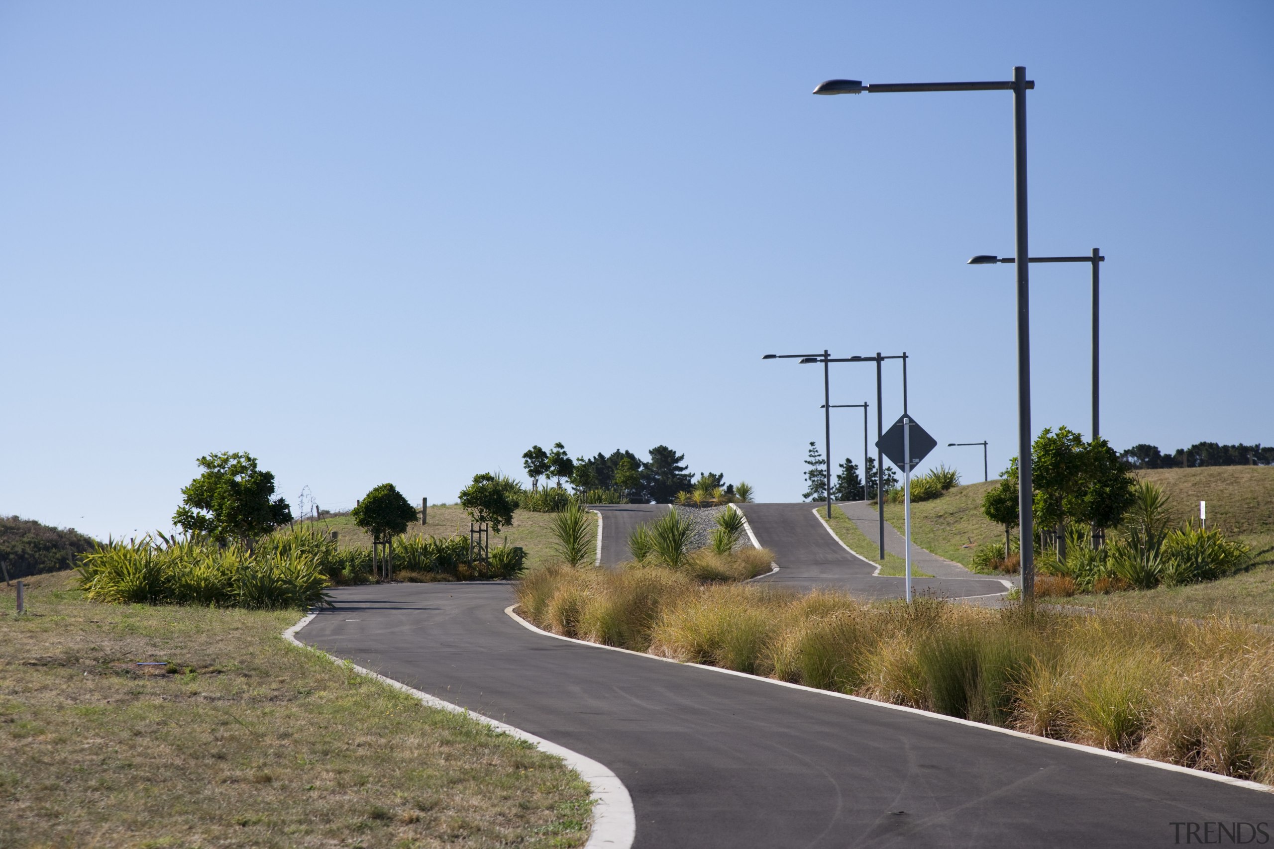 View of surrounding landscape of a energy-efficient development. asphalt, field, grass, infrastructure, land lot, lane, road, road surface, rural area, sky, street light, tree, teal
