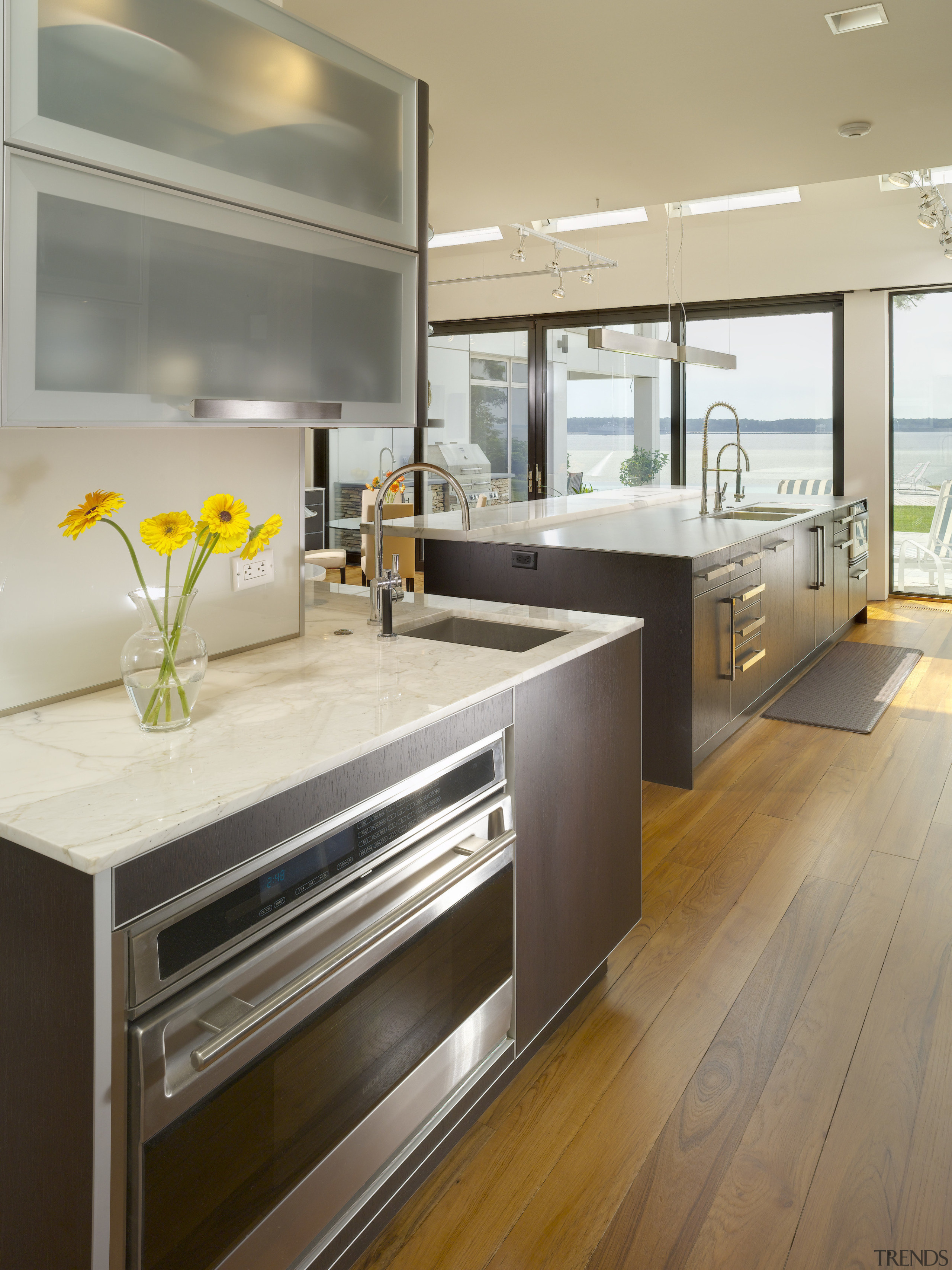 View of contemporary kitchen which features island, stainless cabinetry, countertop, floor, flooring, interior design, kitchen, wood flooring, gray, brown