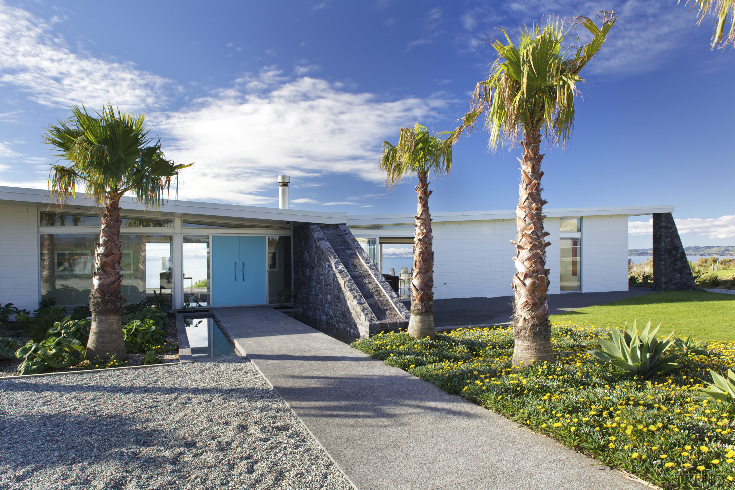 ​​​​​​​On the approach, this house presents pristine white architecture, arecales, building, daytime, estate, facade, home, house, landscape, palm tree, plant, property, real estate, residential area, sea, sky, tree, vacation, blue