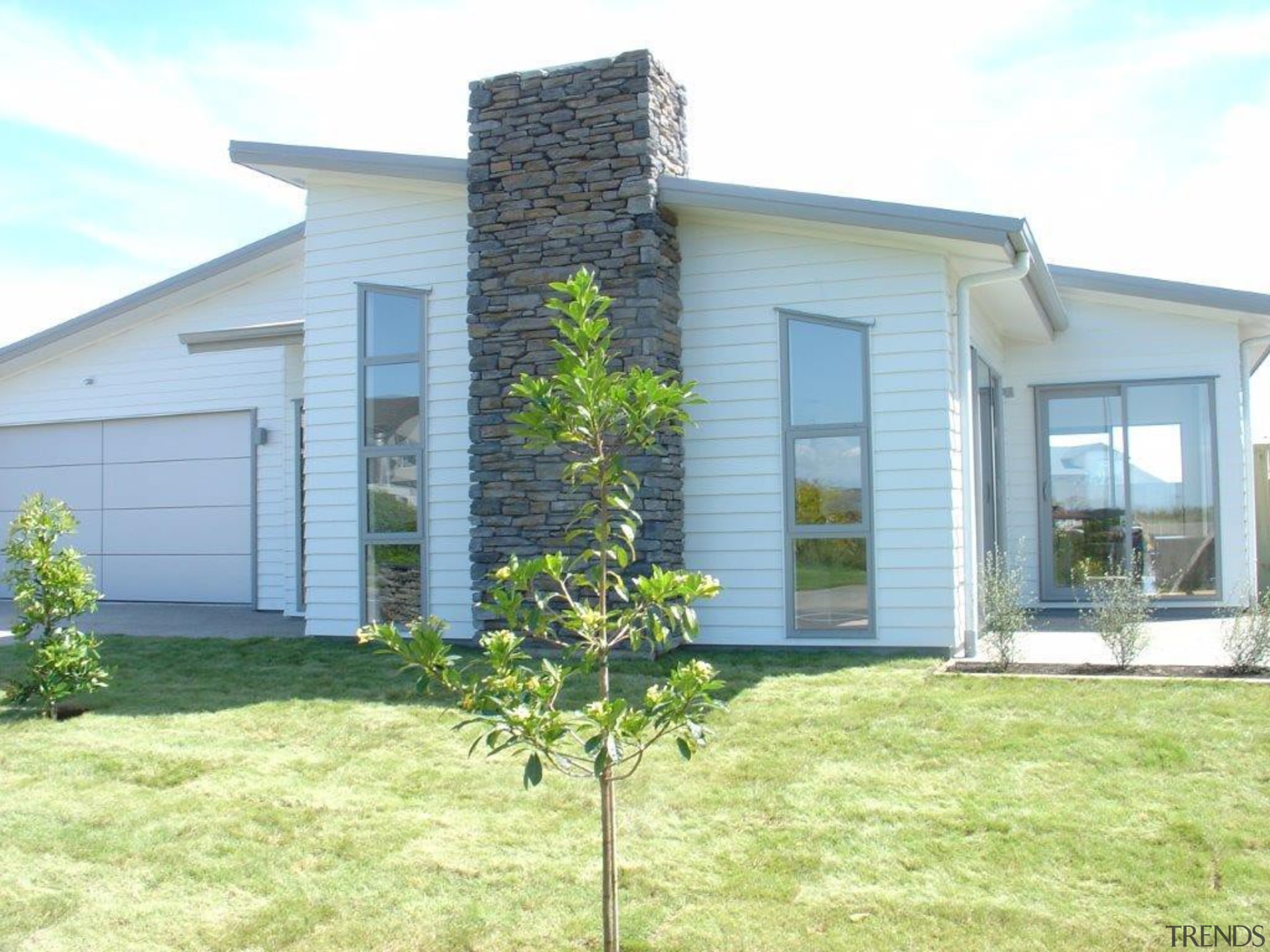 This contemporary home has a stone feature chimney cottage, estate, facade, grass, home, house, land lot, property, real estate, siding, window, yard, white, yellow