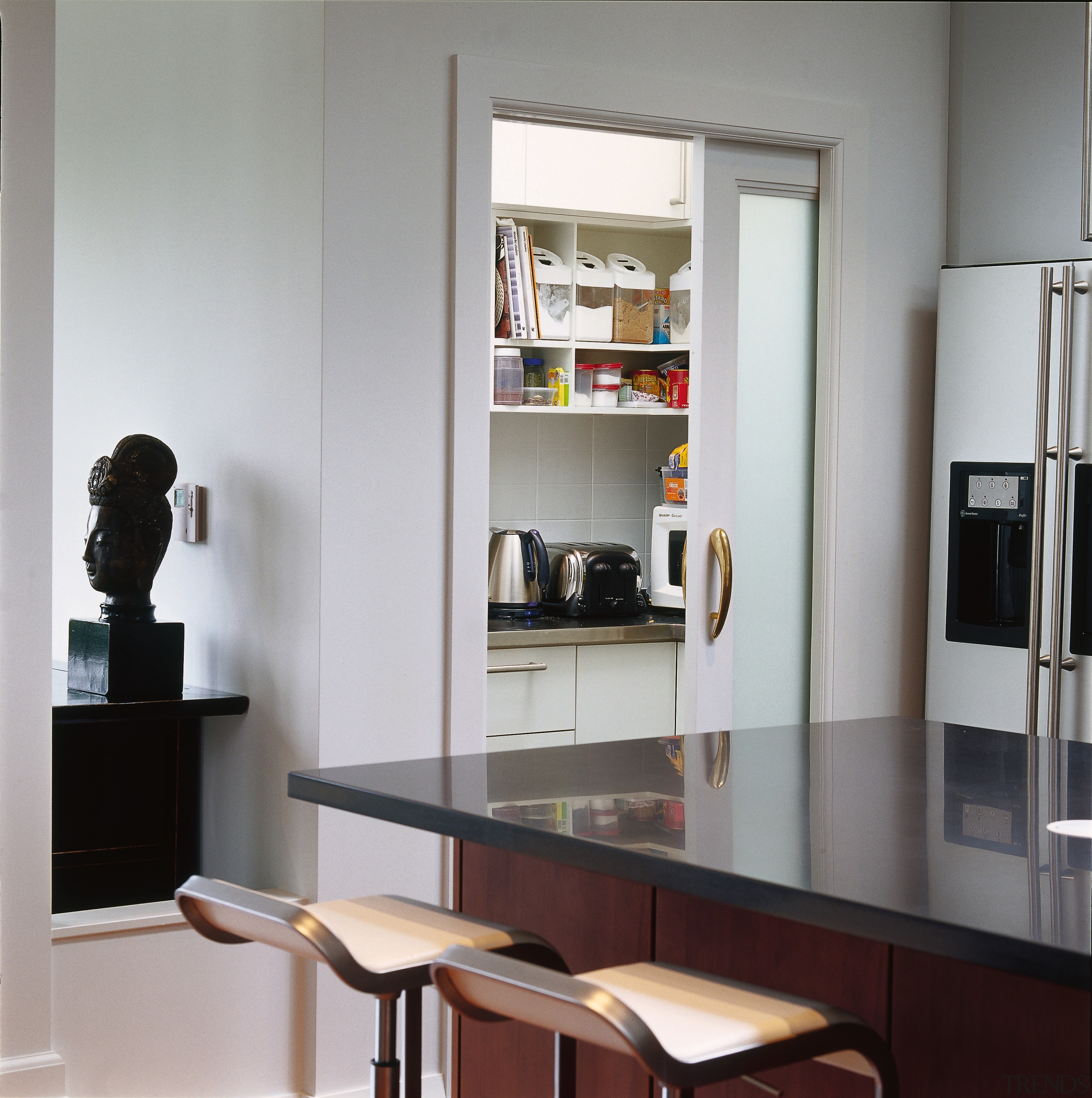 Bar stools at wide dark kitchen island, with bookcase, furniture, interior design, product design, shelf, shelving, table, gray
