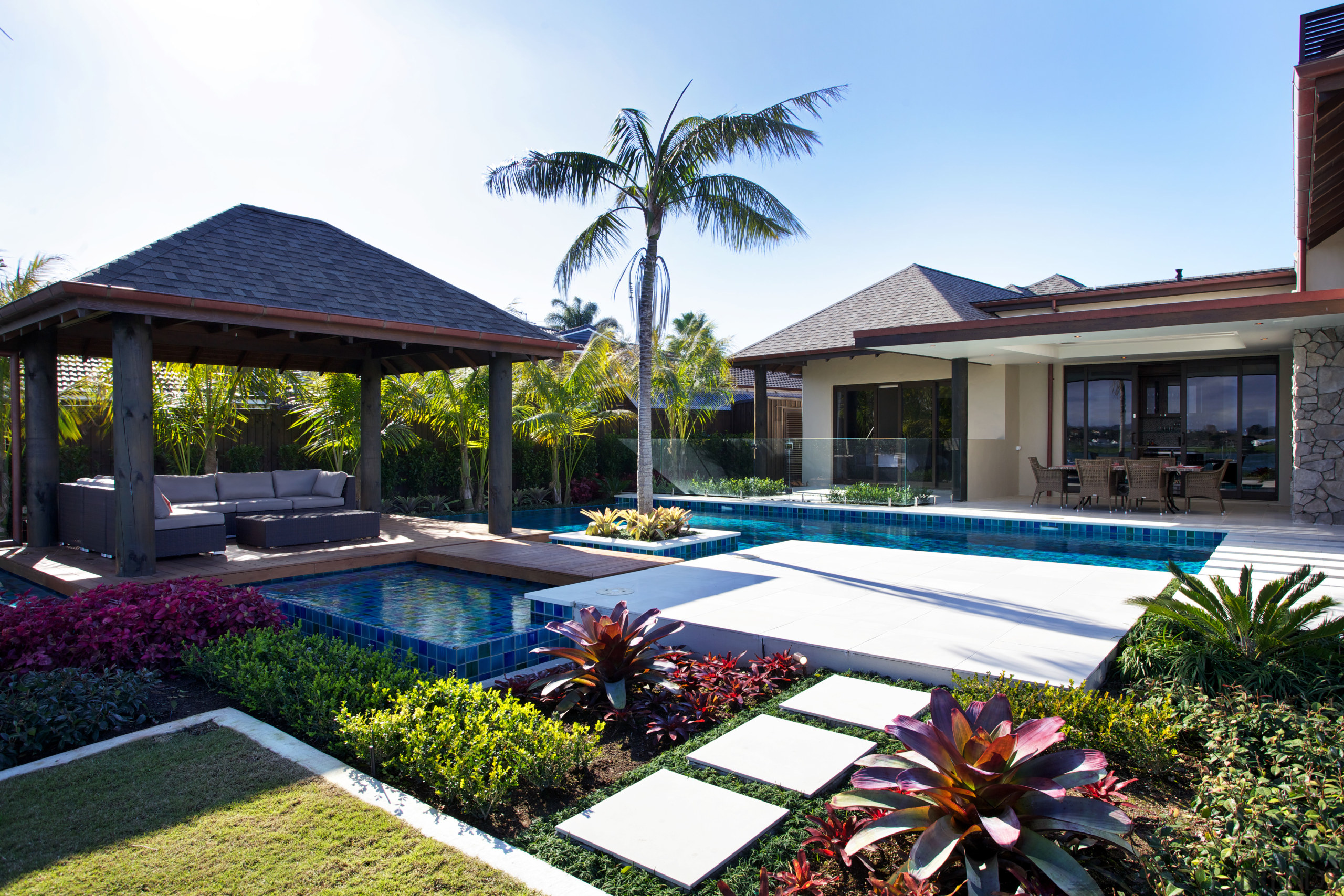 The architecture of this house is enhanced by backyard, cottage, estate, home, house, landscaping, leisure, palm tree, property, real estate, residential area, resort, swimming pool, villa, white