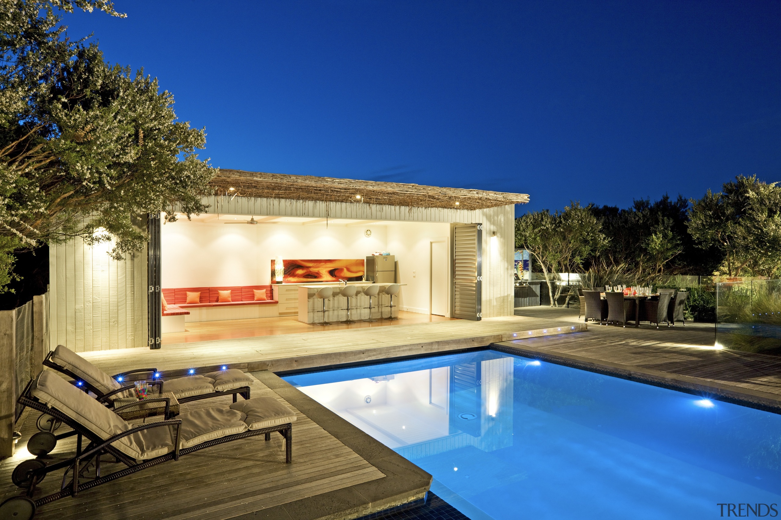 Evening view of the poolside living area - architecture, backyard, cottage, estate, home, house, lighting, property, real estate, residential area, sky, swimming pool, villa, blue, brown