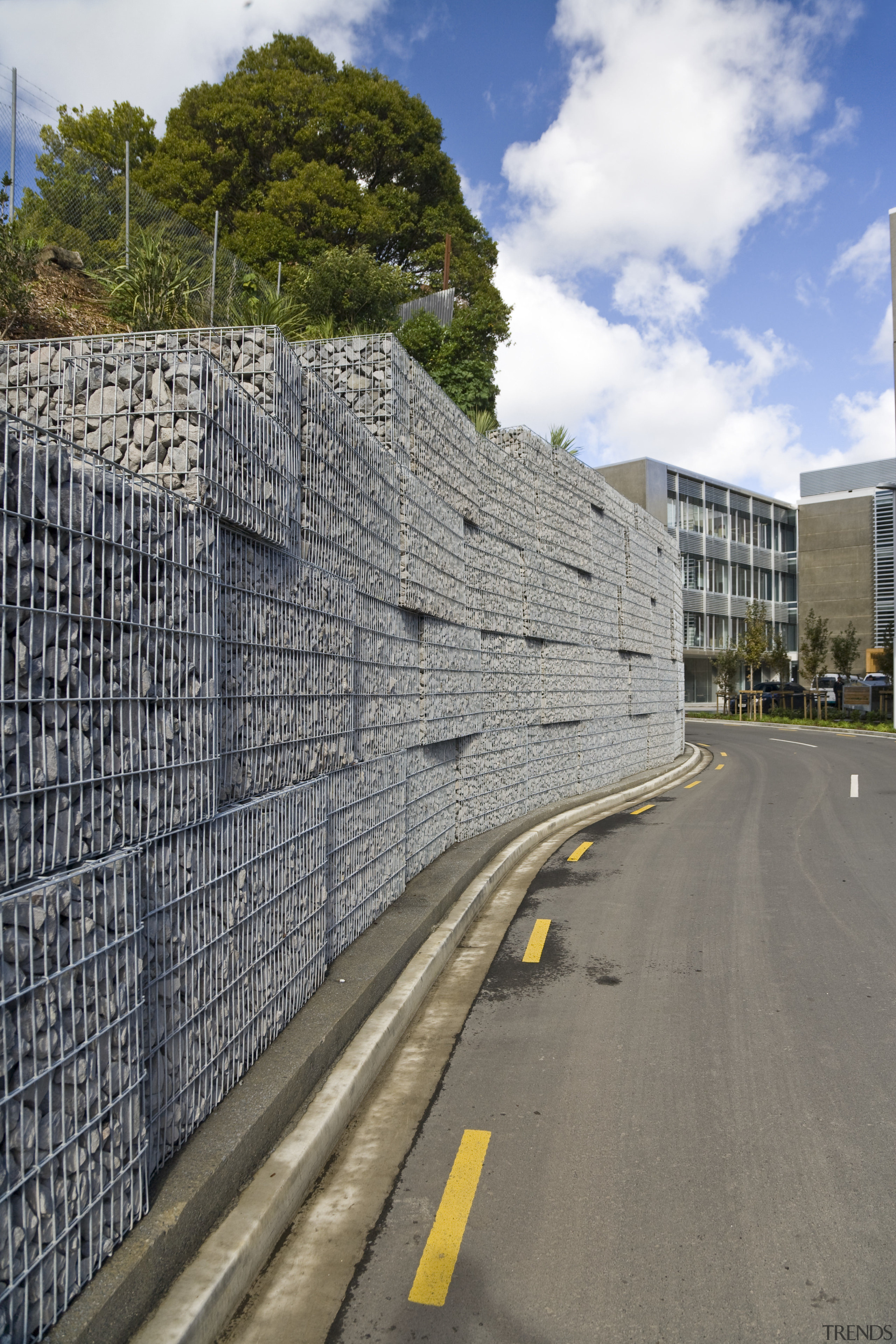 View of a large retaining wall with a architecture, asphalt, building, facade, house, infrastructure, landmark, lane, metropolitan area, residential area, road, road surface, sky, structure, urban area, wall, gray