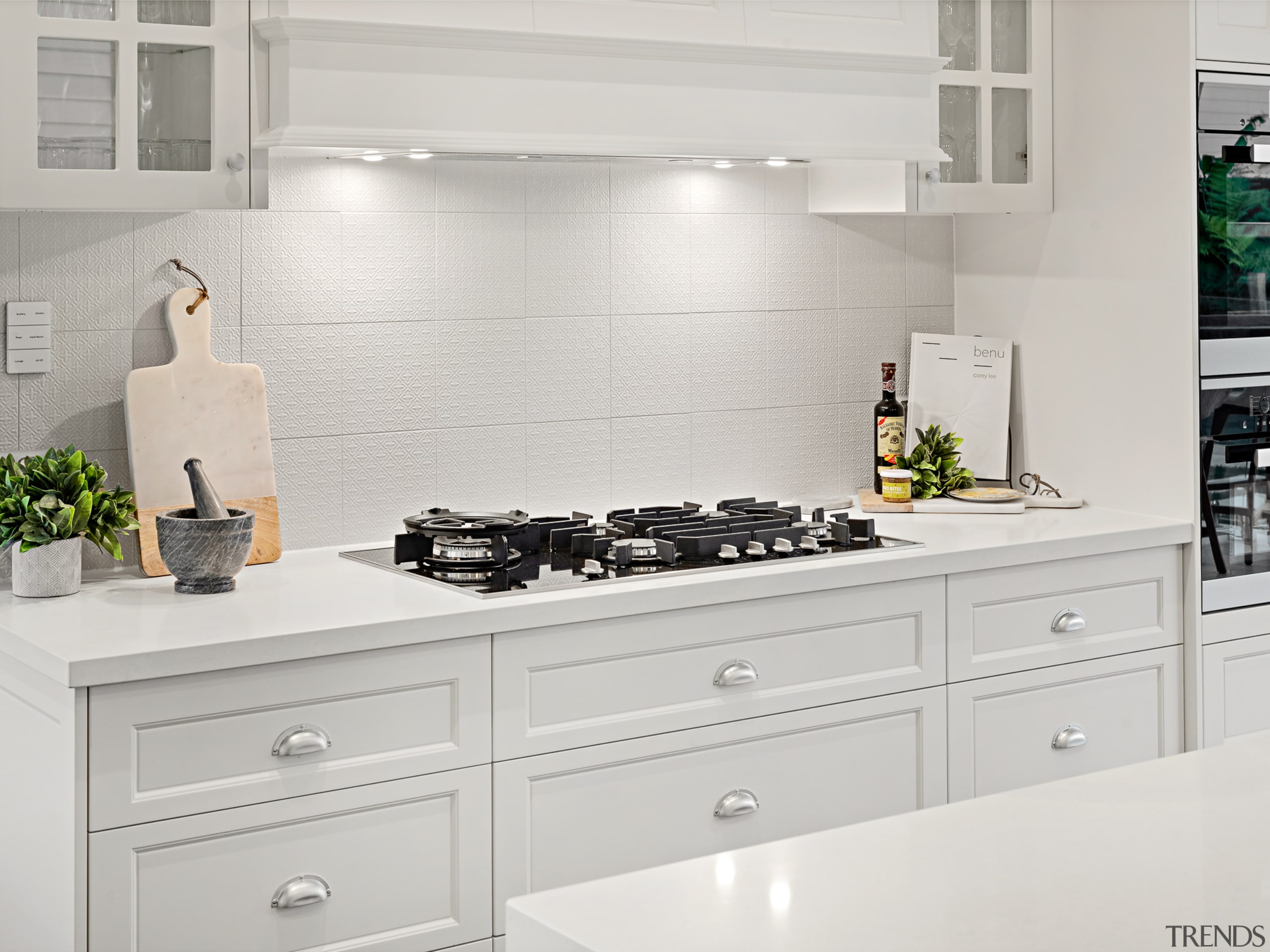 ​​​​​​​Set directly behind the feature island in this cabinetry, furniture, cooktop, kitchen, kitchen appliance, major appliance, tile, white