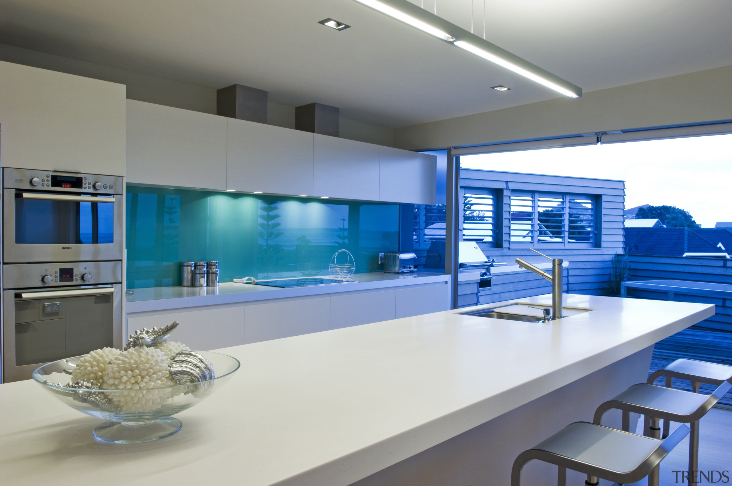 This sleek kitchen in a beach house features architecture, countertop, glass, interior design, kitchen, gray