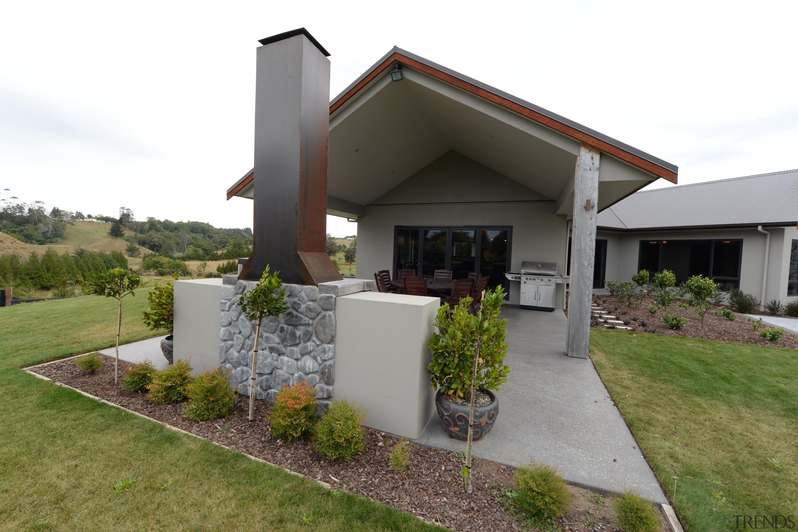 Loggia featuring a Trenz Outdoors open fireplace.Built by architecture, cottage, facade, home, house, landscape, property, real estate, yard, white, brown
