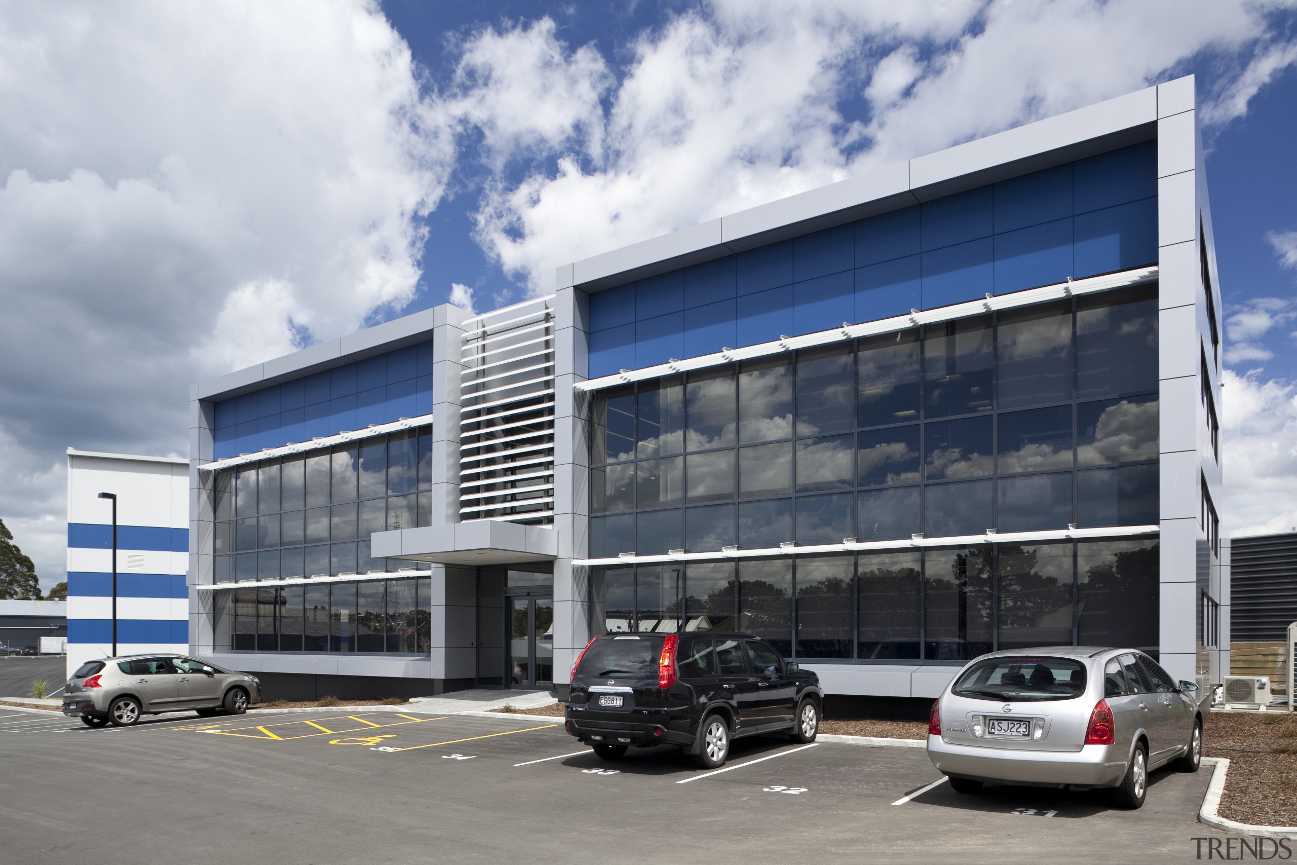 View of exterior with cars parked in front. architecture, building, car, car dealership, commercial building, corporate headquarters, facade, family car, headquarters, luxury vehicle, metropolitan area, mixed use, real estate, sky, vehicle, gray, white